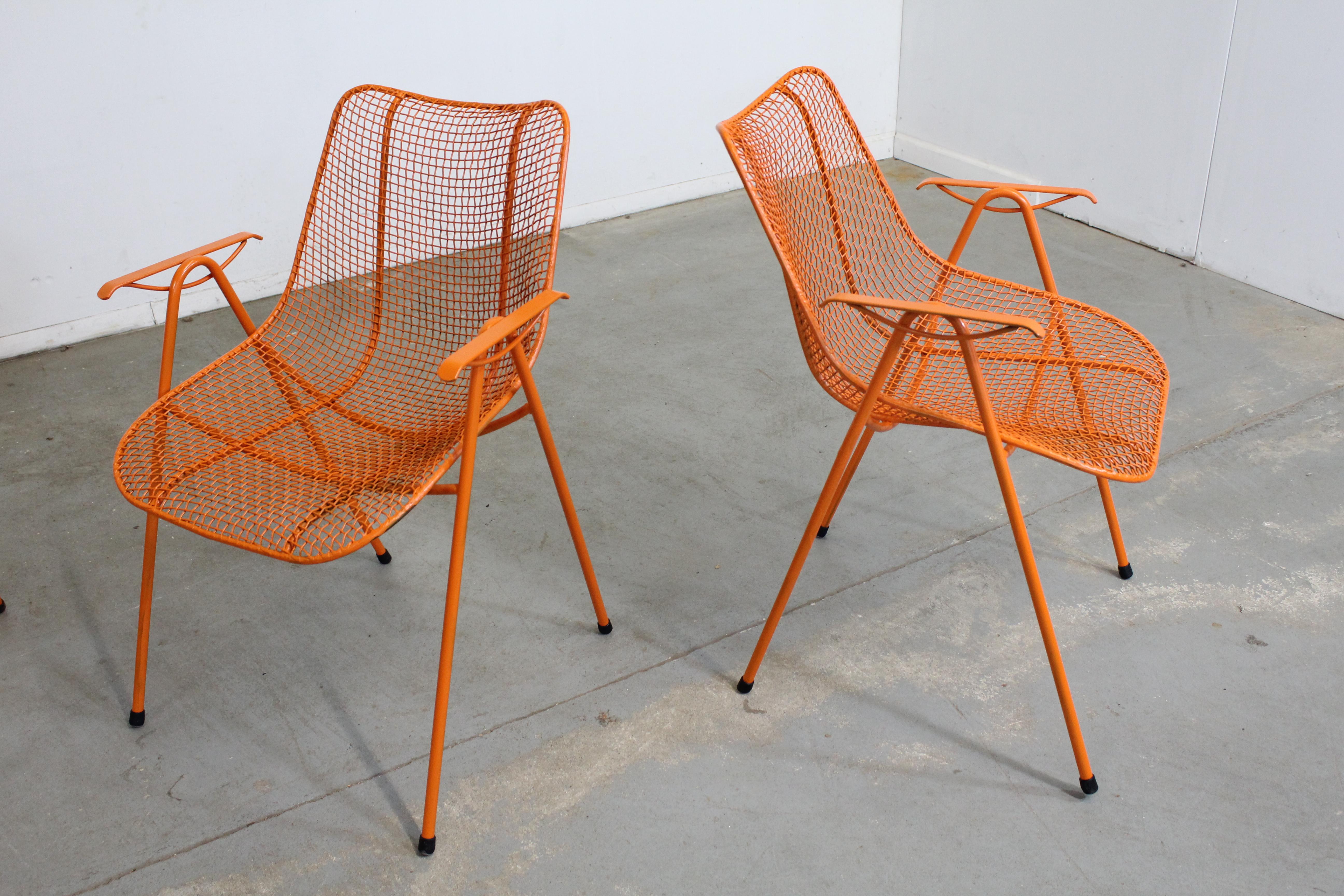 Offered is a set of 4 Mid-Century Modern outdoor arm chairs designed by Russell Woodard (circa 1956) for the 'Sculptural' line. Features enameled and woven wrought iron. The chairs are structurally sound, in very good condition with new orange