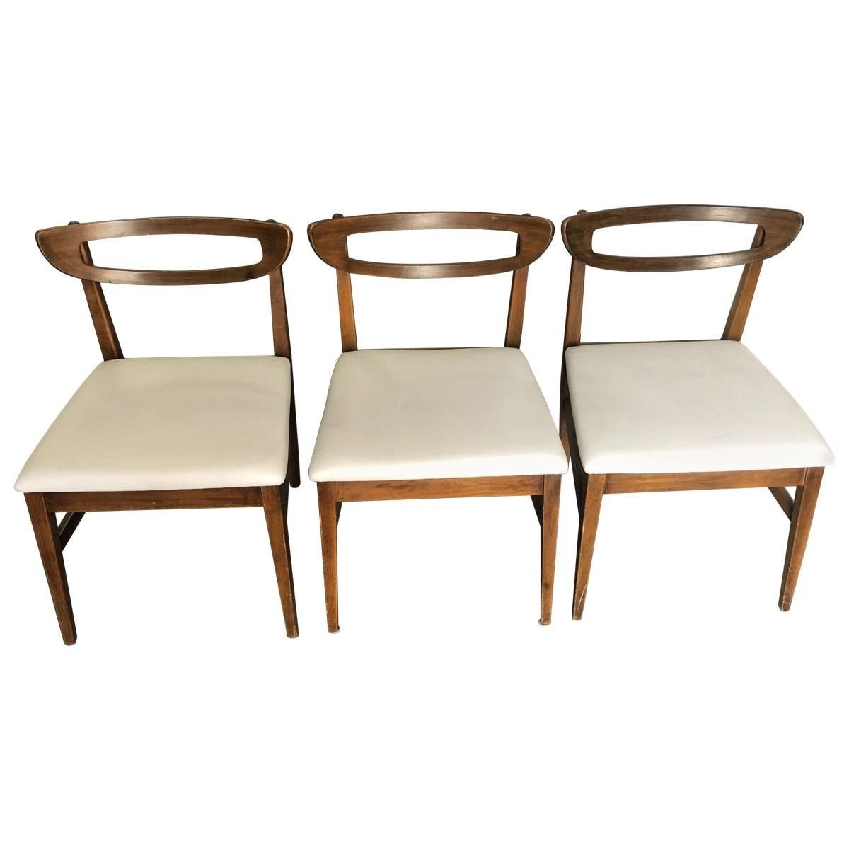 Sleek and shapely, this eye-catching set of four plywood dining chairs includes three side chairs and one armchair. Rounded open top rails and white vinyl seats give these Mid-Century Modern dining chairs added sophistication.
 