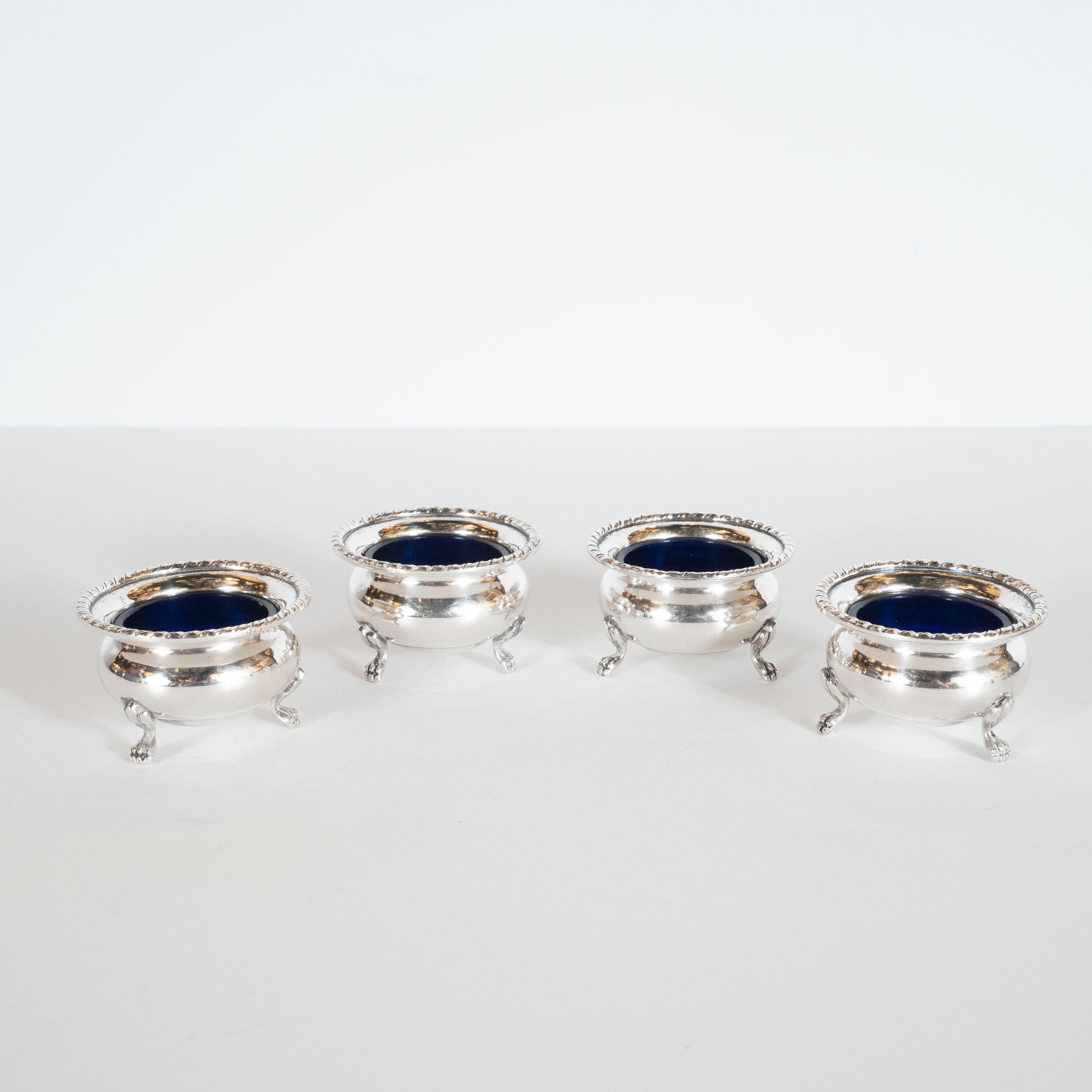 This elegant set of neoclassically inspired salt cellars were produced in Great Britain, circa 1950. They features undulating bodies full of graceful curves with a circular braided lip. They rest on three claw feet with stylized acanthus detail at