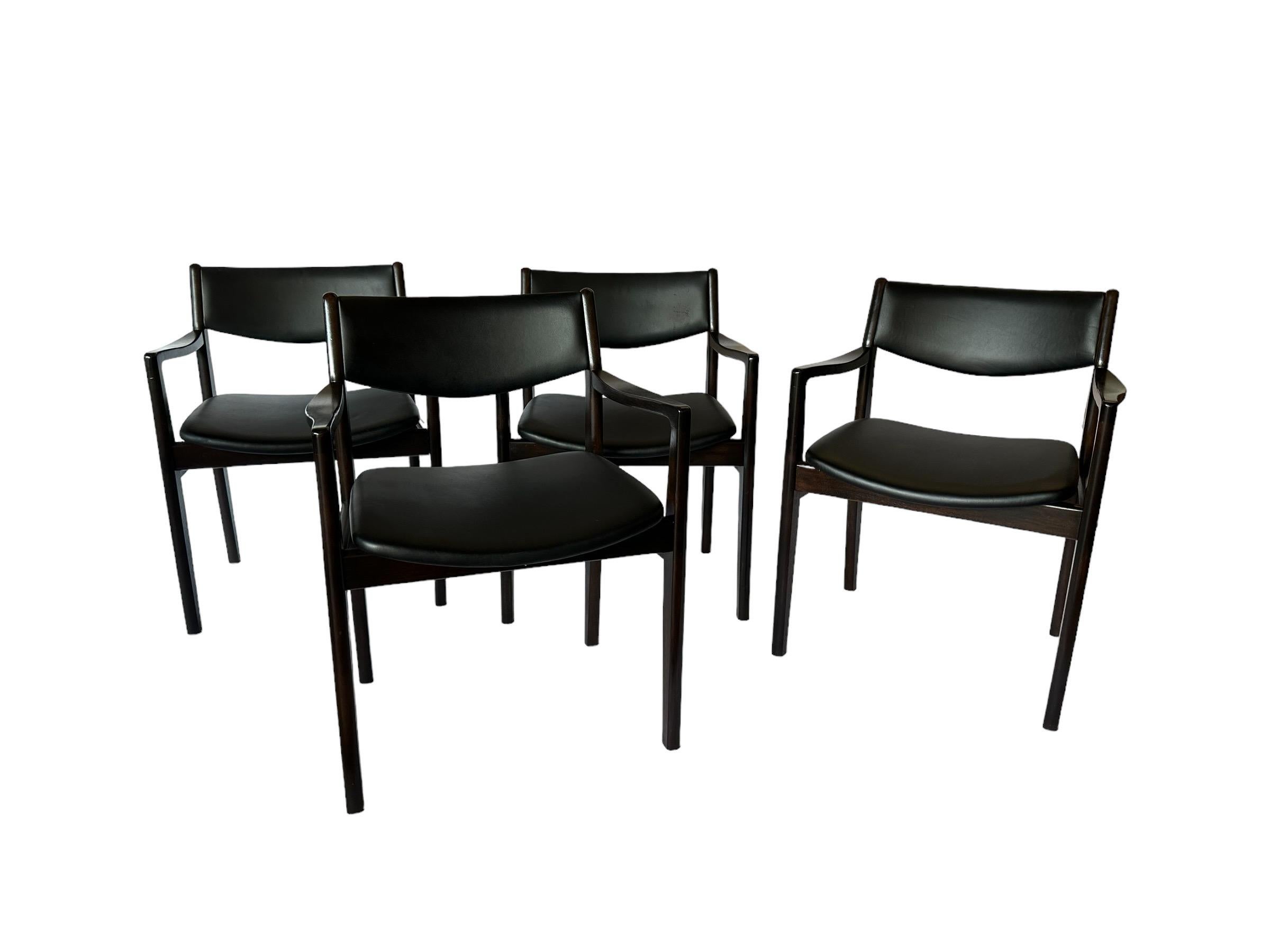 Set of four midcentury modern dining chairs. All matching chairs constructed of hardwood and evenly toned to a dark rosewood hue. Original naugahyde upholstery dyed black. In overall even condition. No tears in the textile or breaks in the wood.