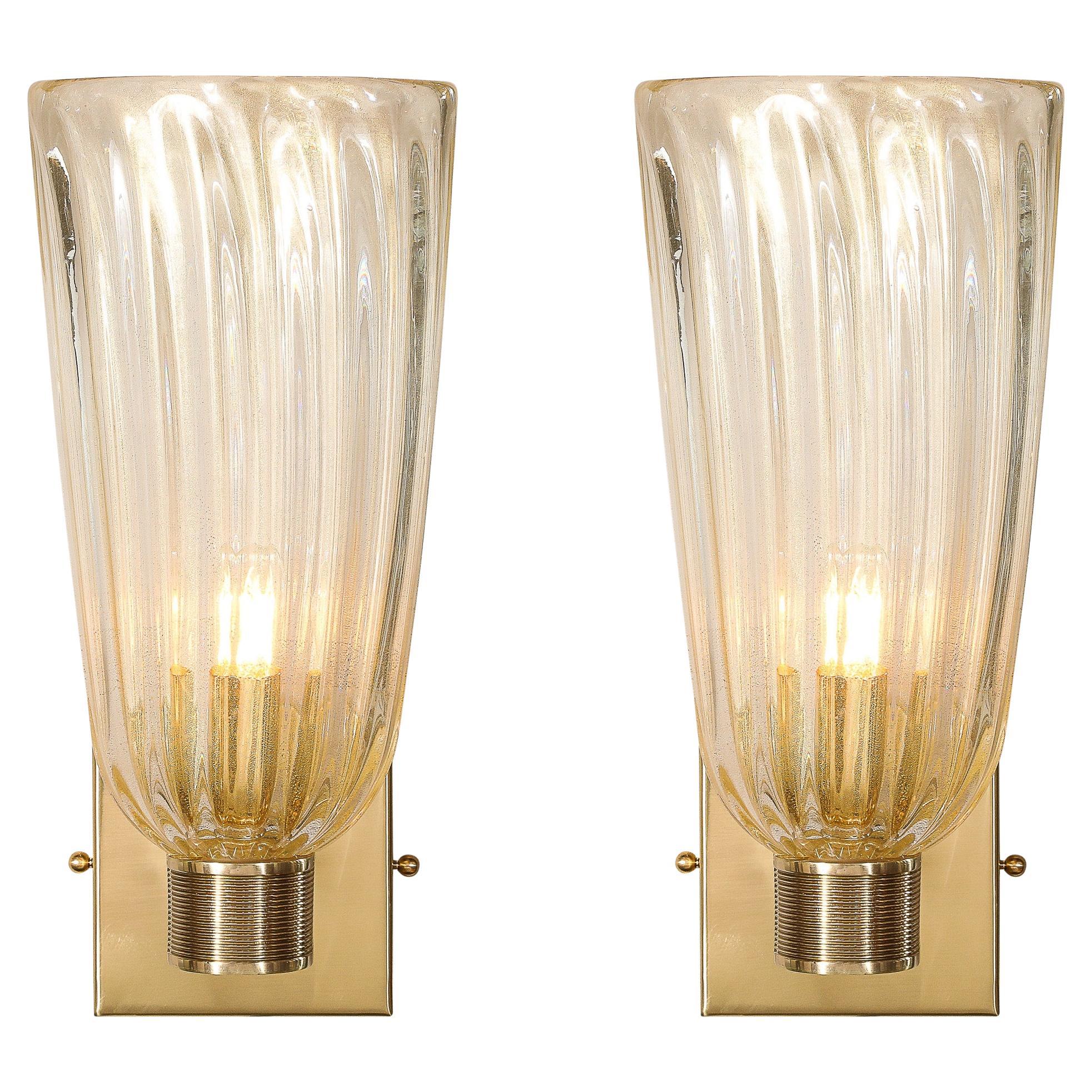 This glamorous Set of Four Modernist Transparent Hand-Blown Murano Fluted Glass Sconces W/ 24kt Gold Flecks originates from Italy during the 21st Century. They feature a fluted shade rendered in transparent glass with 24kt Gold Flecks carefully