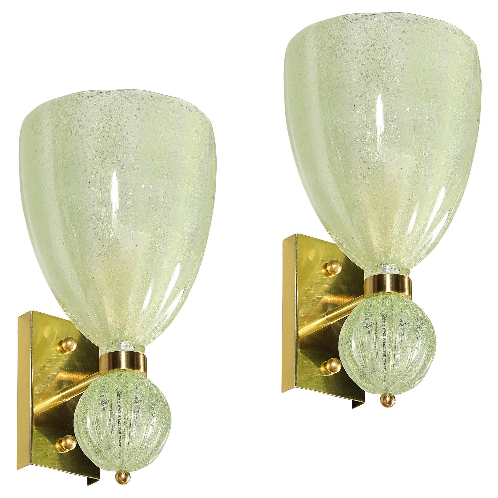 Questo elegante set di quattro applique moderniste in vetro di Murano soffiato a mano, realizzate in Italia nel XXI secolo, presenta una deliziosa tonalità verde giada pallido che dona un tocco di serenità a qualsiasi ambiente. Il vetro dalla