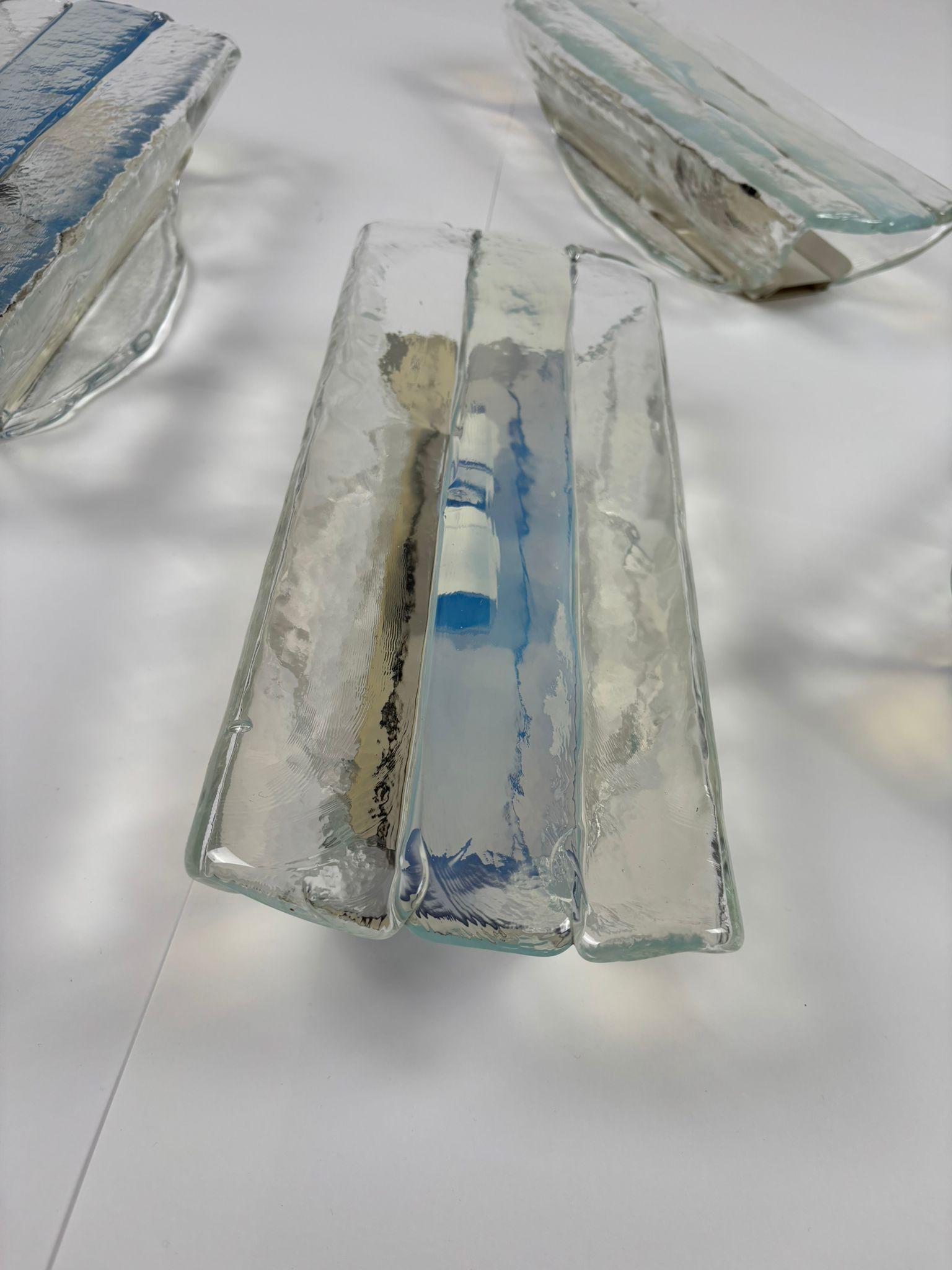 A set of four wall lamps (appliques) designed by renowned designer Carlo Nason and produced by Mazzega in the 1970s. Crafted from clear Murano glass, each lamp features elegant blue shades and a white metal support, creating a sophisticated color