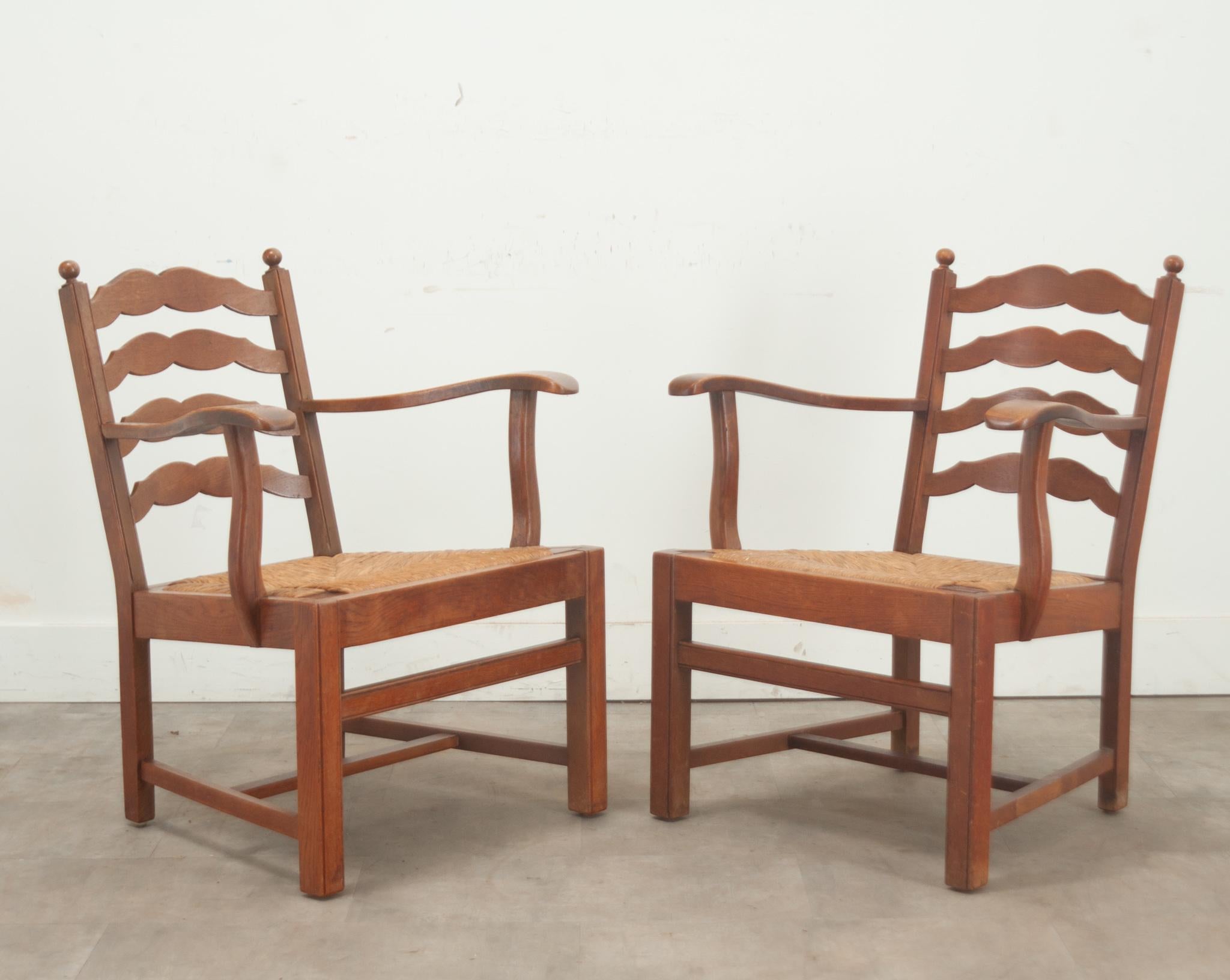 A comfortable set of solid oak and rush seat ladder back lounge chairs. This set of chairs are made of solid oak frames with scalloped ladder backs and long sloping arms. The rush seats are removable and the seat slopes back for a lounge like