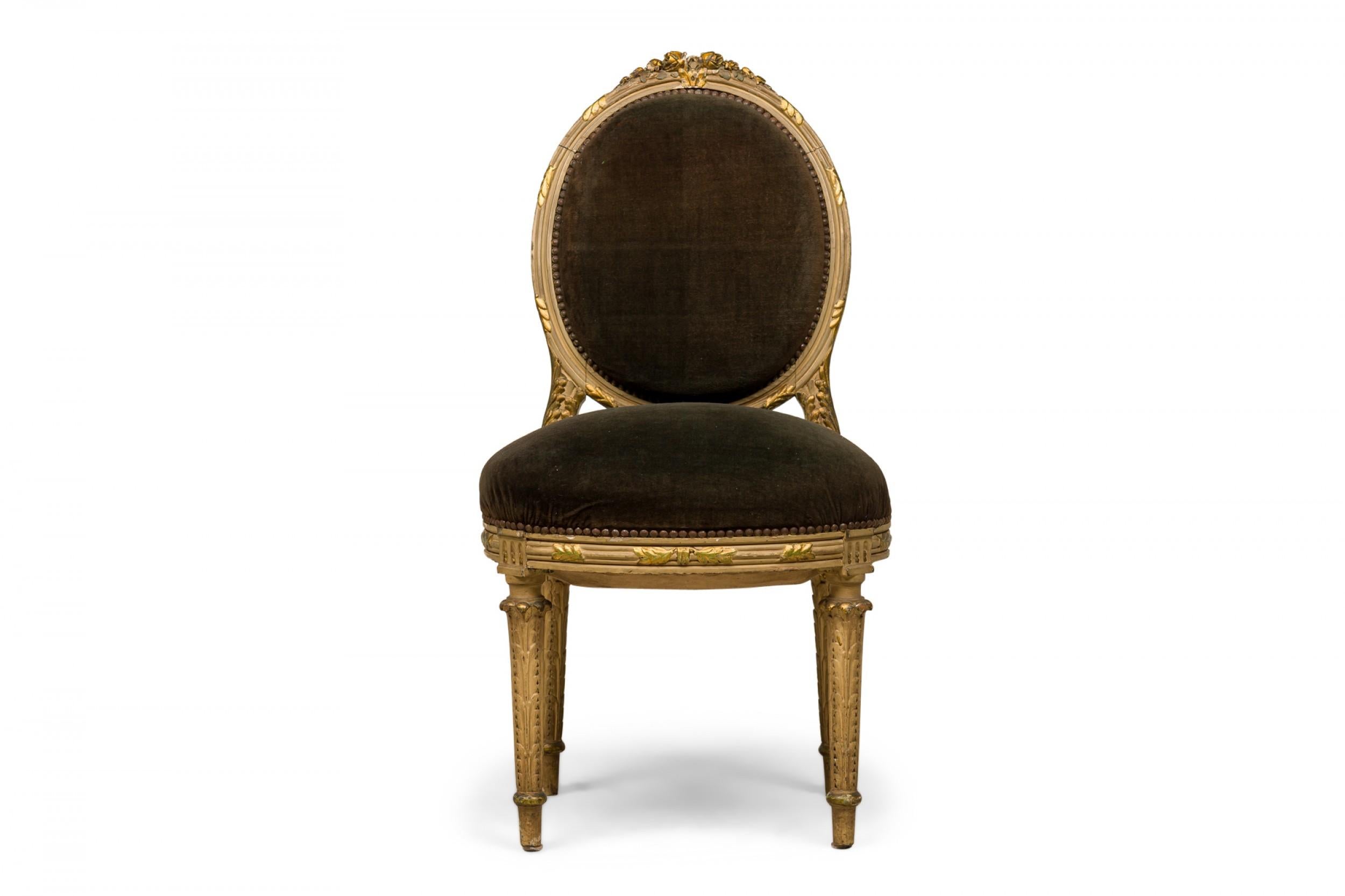 Set di 4 sedie da pranzo francesi in stile Luigi XVI (19/20° secolo) con schienali ovali imbottiti in velluto verde, decorazioni con chiodi e strutture con finitura verniciata grigia e dorata con motivo a foglie intagliate sormontate da creste di