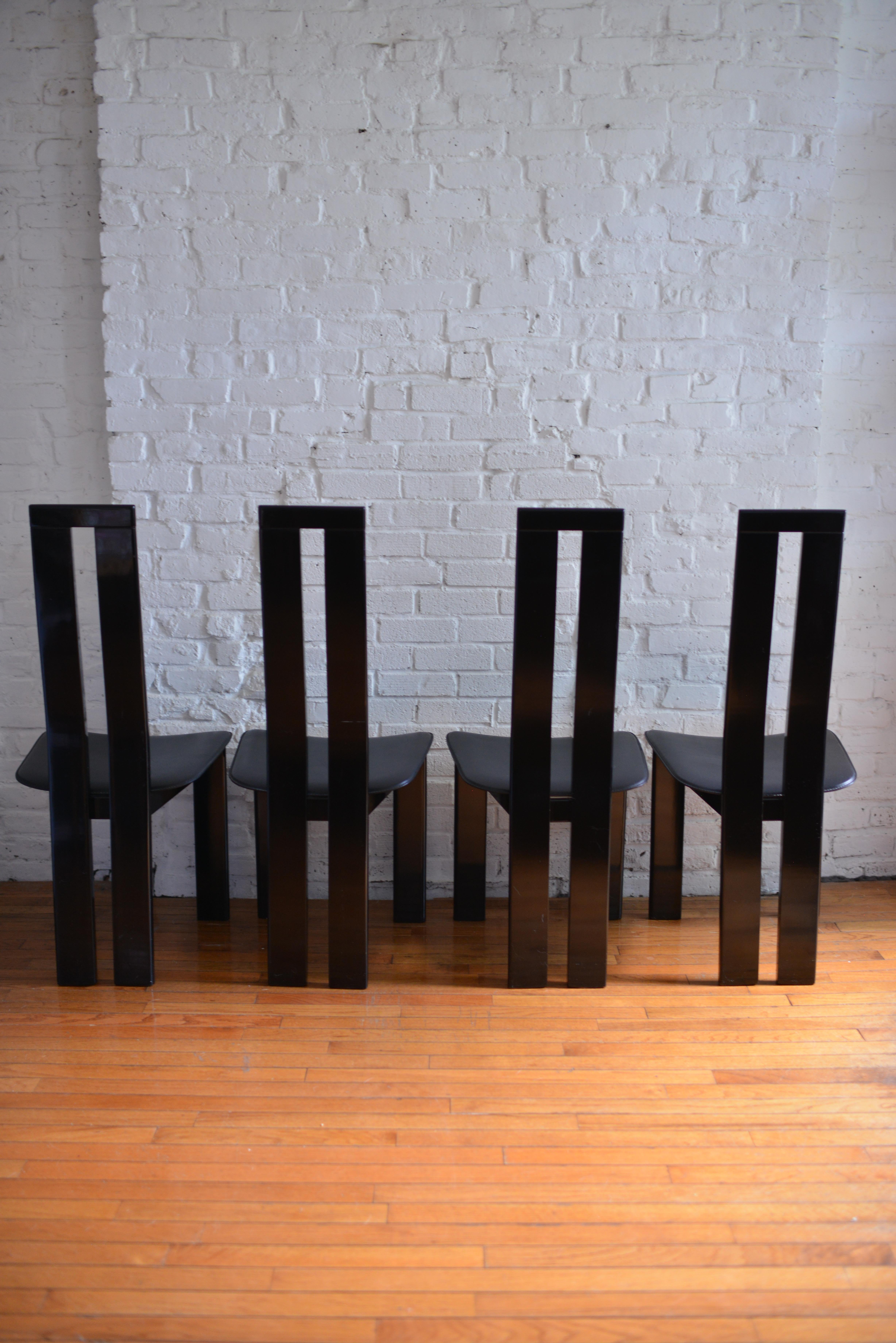 Set of four dining chairs designed by Pietro Costantini for Ello. The chairs feature black lacquered wood, a sculptural piano back and stitched black saddle leather seats. The chairs are highly comfortable with their slightly scooped seats. Made in