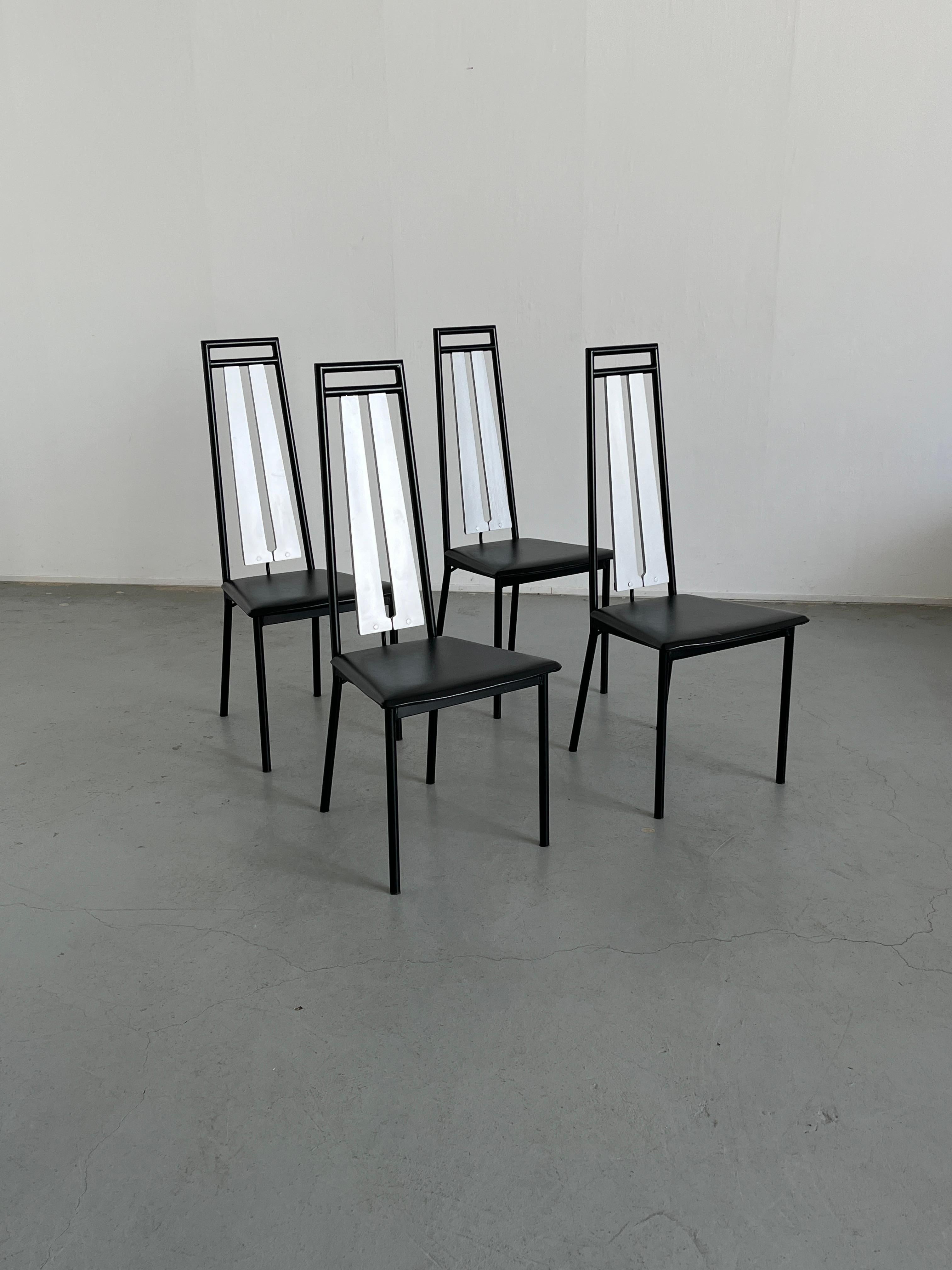 Ensemble de quatre chaises de salle à manger à dossier haut brutaliste en métal noir et faux cuir avec un élément de dossier en bois argenté. Production italienne postmoderne classique des années 1980.

Les chaises sont en excellent état vintage