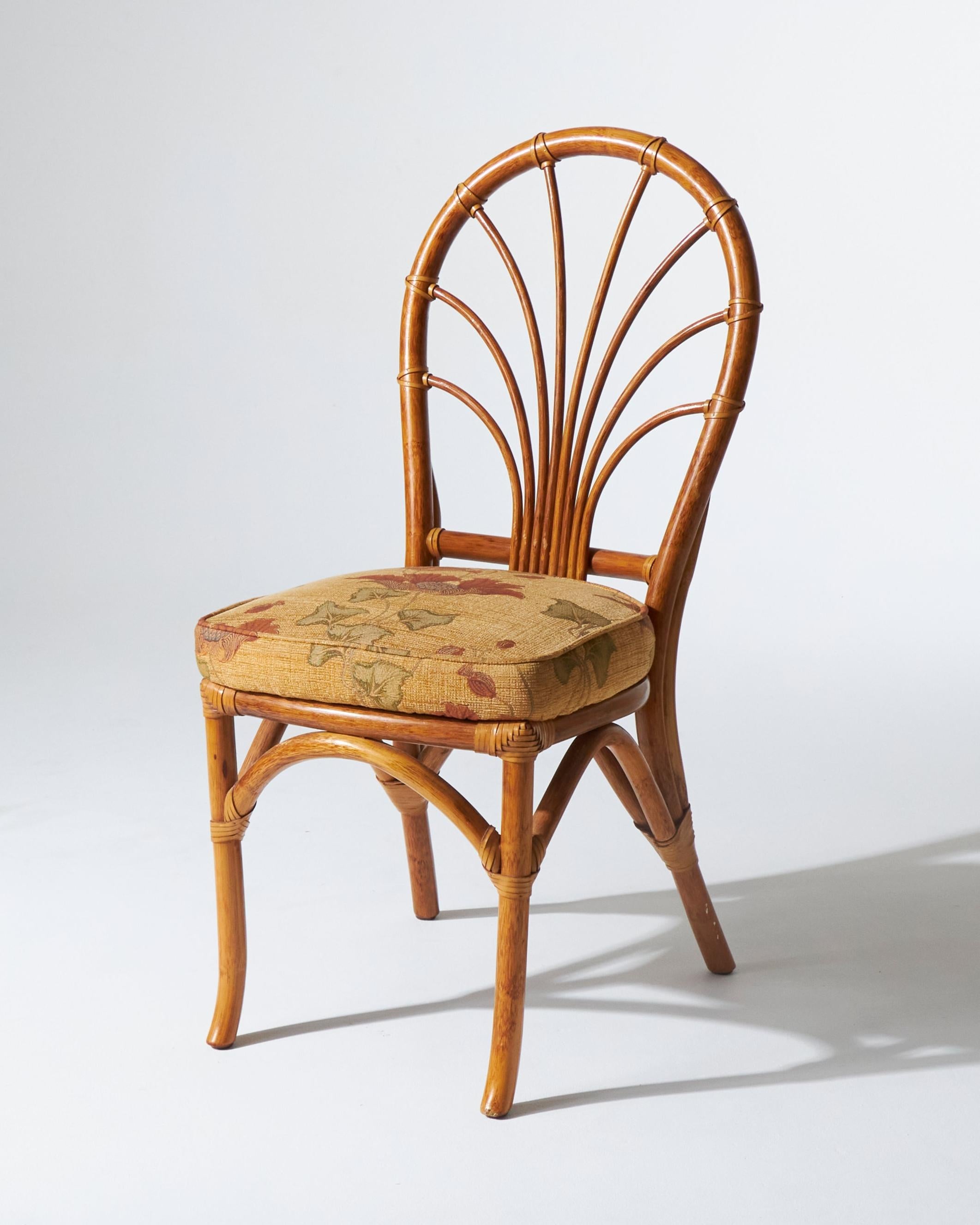 Lot de 4 chaises en rotin de style bambou, aux pieds légèrement évasés et aux dossiers ajourés, chacune équipée d'un coussin à motifs floraux. Convient comme chaise de salle à manger ou dans un salon d'été. En bon état général. Label Maugrion,