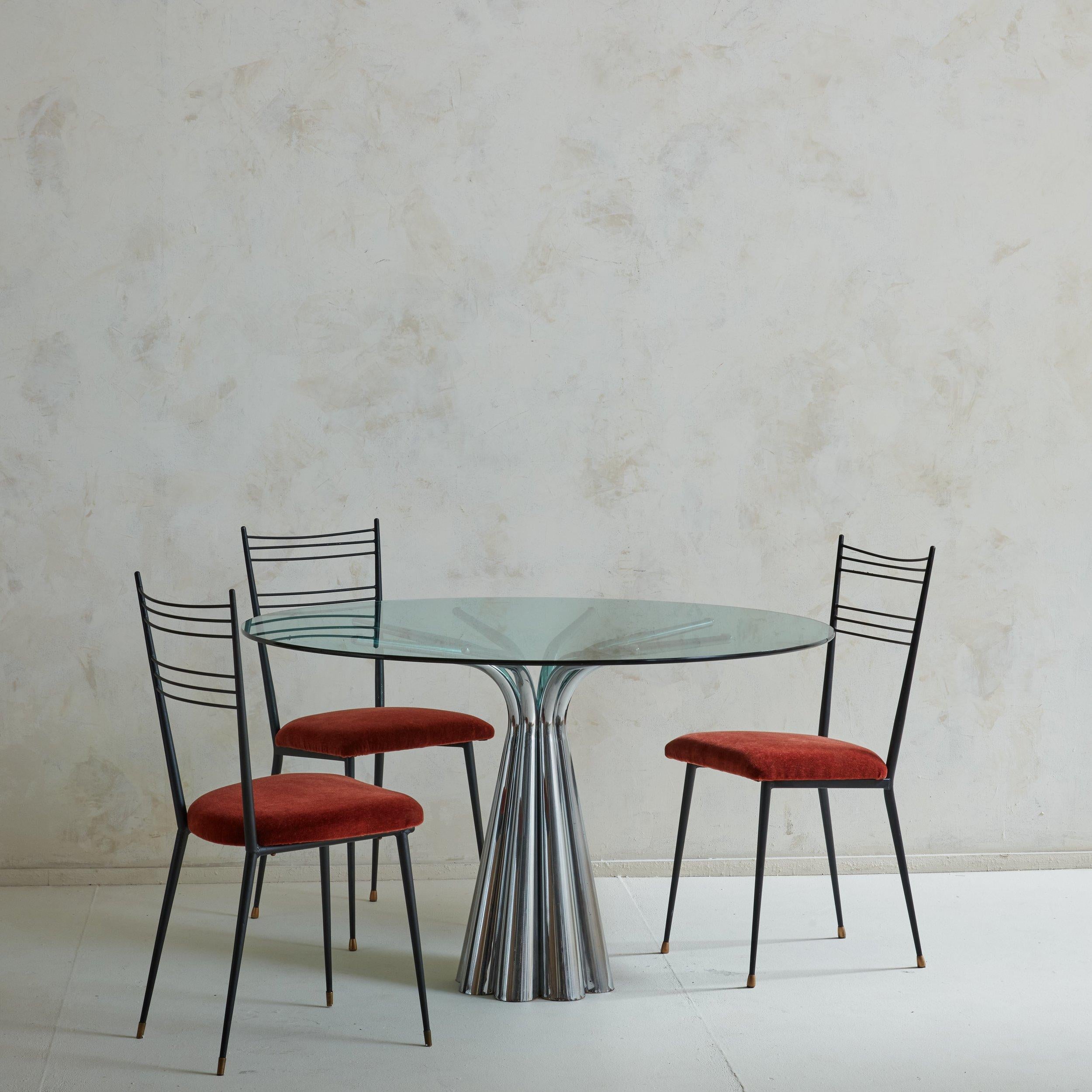 A set of 4 Mid Century French dining chairs attributed to Colette Guedon. These chairs feature sleek black enameled steel frames with tapered legs and patinated brass sabots. The seat backs are composed of six horizontal rods which have a subtle