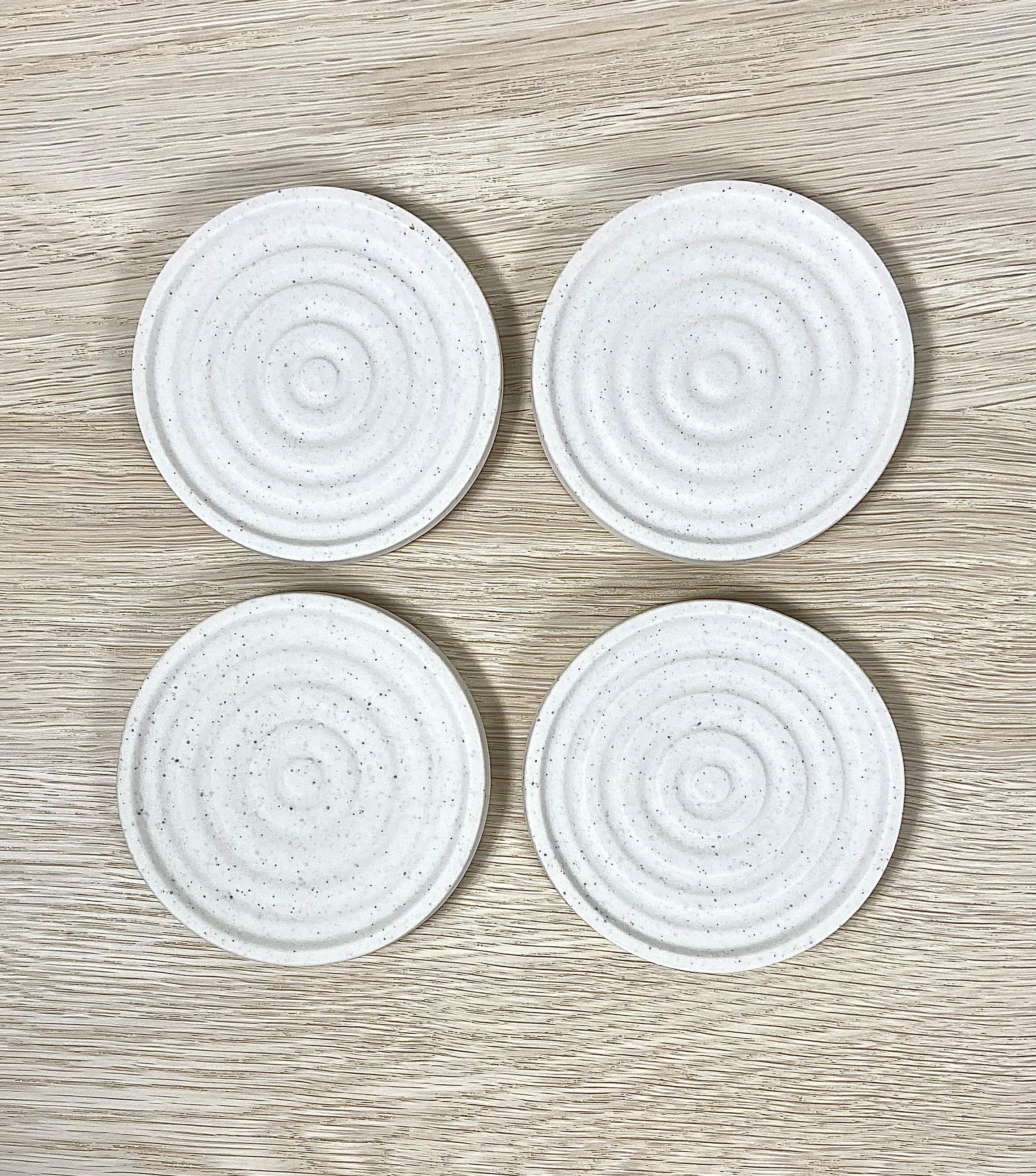 A set of 4 porcelain coasters with a speckled swirl pattern. The ivory coasters have a cork bottom to protect your surfaces and also stack neatly on top of one another. A stylish and modernist set that looks great in any interior, be it modern or