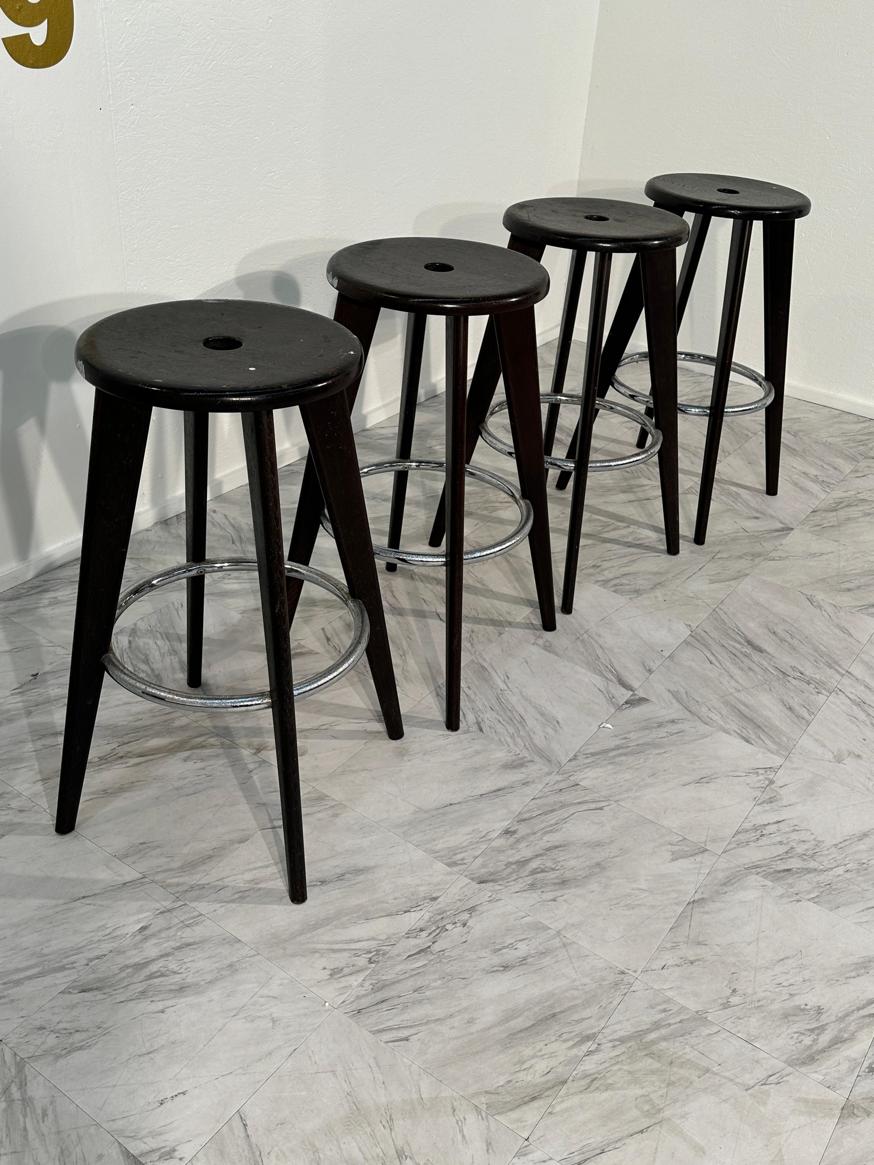 The Set of 4 Tabouret Haut Jean Prouvé Bar Stools by Vitra in Dark Oak showcases iconic mid-century design with a contemporary twist. Designed by renowned architect and designer Jean Prouvé, these stools feature a sleek and sturdy dark oak