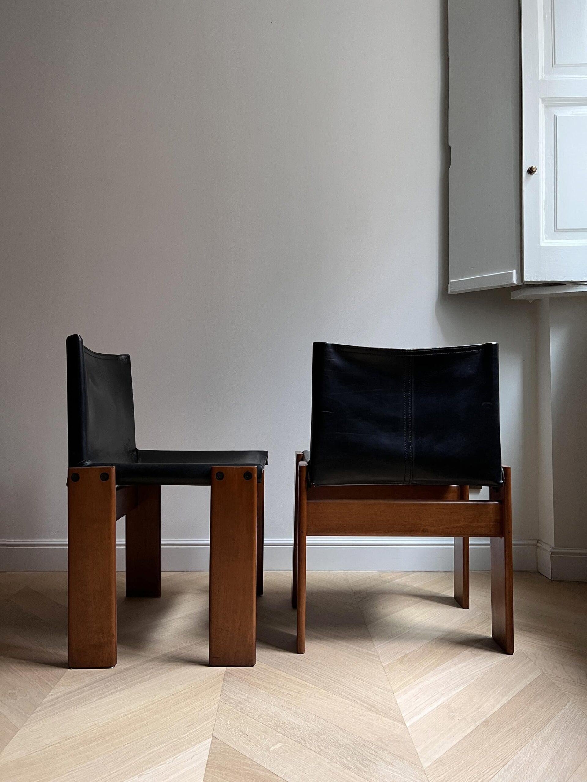 This beautiful set of 4 Scarpa Monk chairs in stunning black patinated leather and wood are unique in the placement of its legs and cross sections, presenting a minimal appearance, whilst concealing the fact that they are extremely solid and