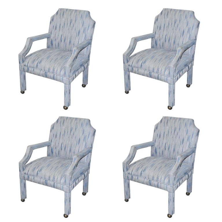 A set of four upholstered rolling chairs with chinoiserie inspired scalloped backs. A mix of Mid-Century Modern and Hollywood Regency, this set of chairs is upholstered in a cool blue flame stitch fabric. The arms are in a geometric shape with