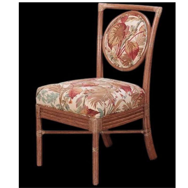 A set of four Mid Century style rattan side chairs with an angular shaped frame and inset with a upholstered circular portion to an open back. Upholstered seat and back are a red, tan and green leaf motif. Chairs have straight legs, reeded rattan
