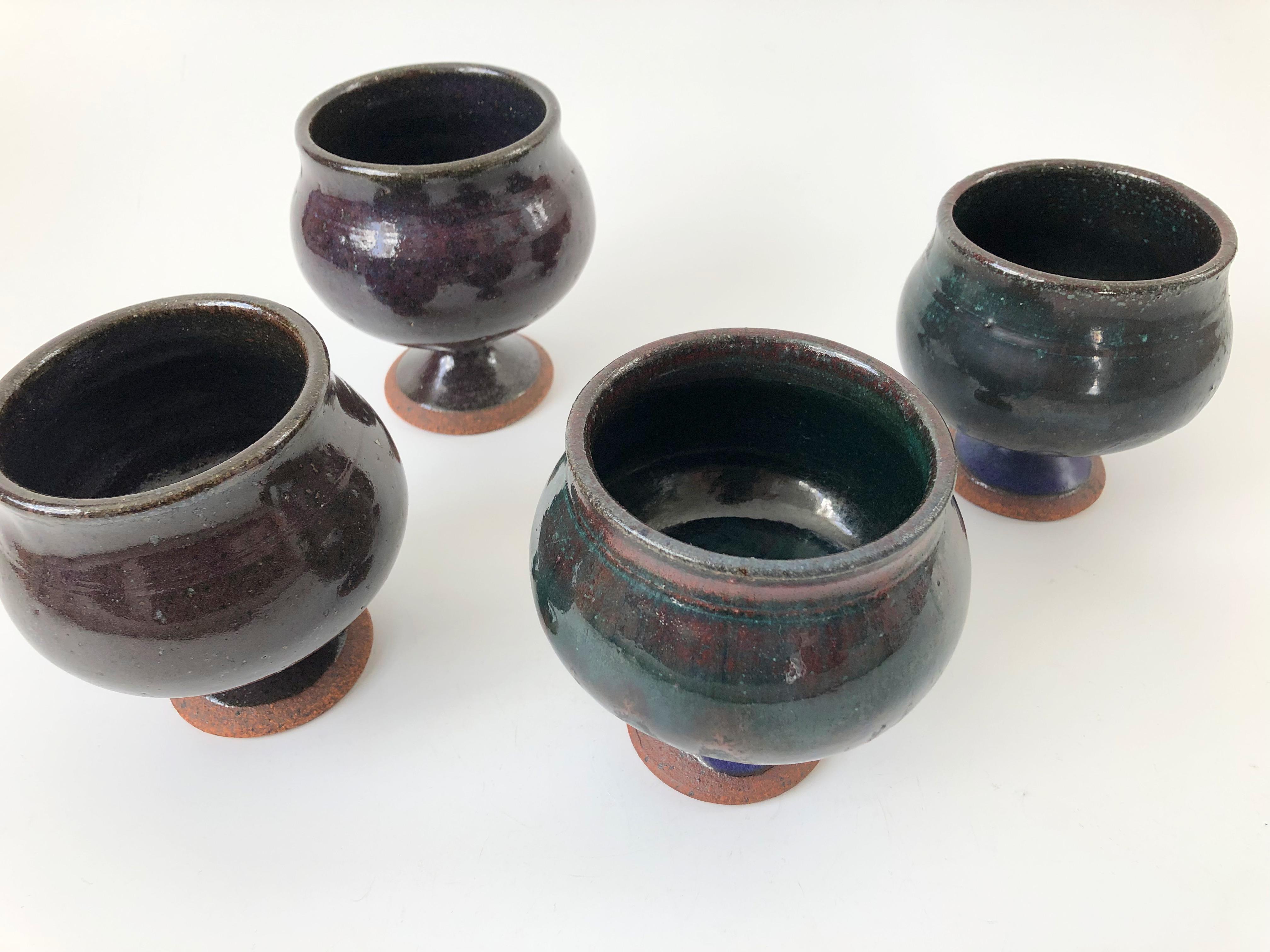 A set of 4 vintage studio pottery goblets. Each with a unique organic shape, standing on pedestal bases. Lovely dark purple and blue tinted glazes. Signed by the maker on the bases and dated 1971.
   