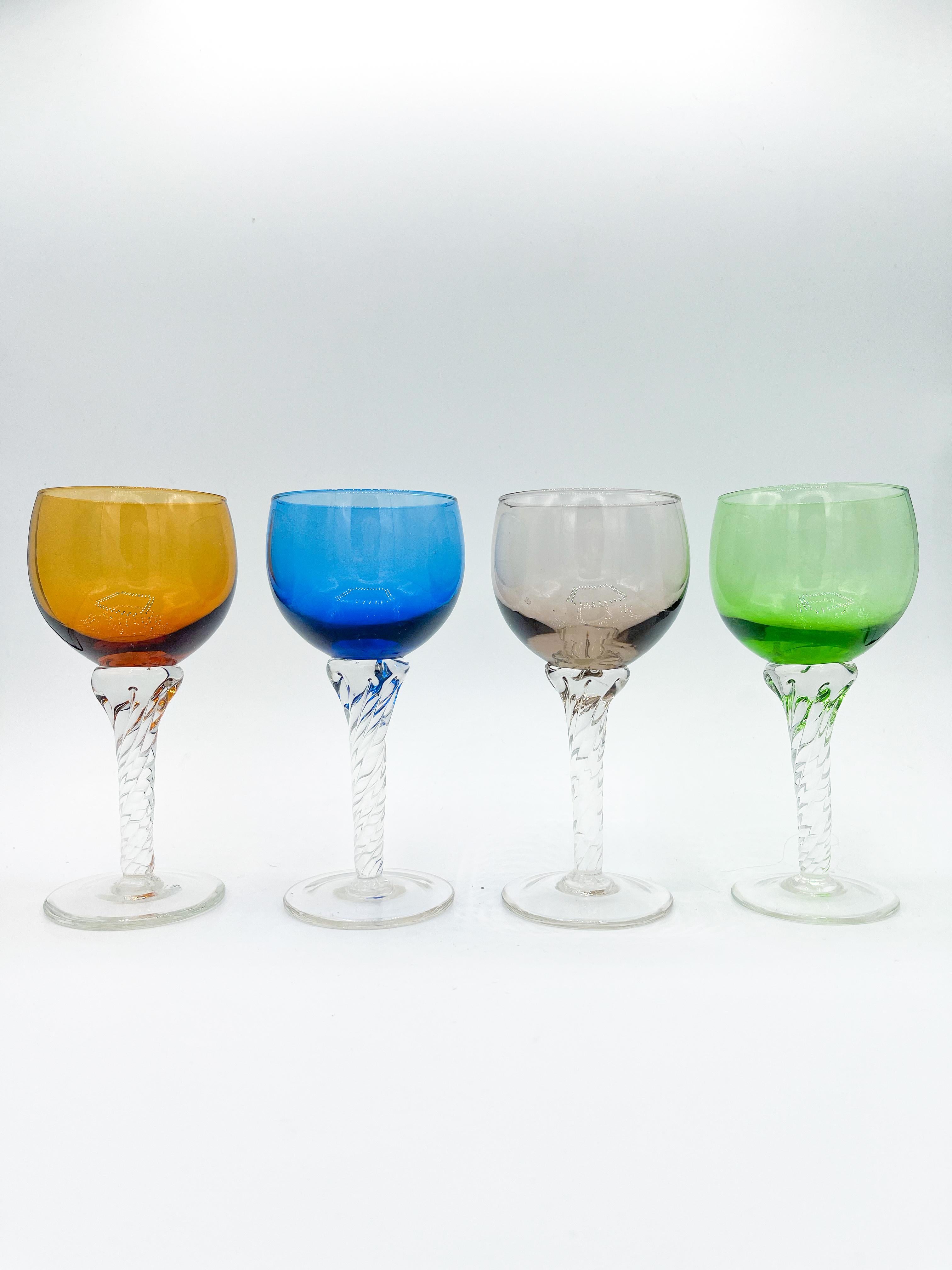 Dating back to the mid-20th century, this set of four vintage Bohemian small wine glasses captures the vibrant style of the 1960s. Each glass features a striking multicolored bowl in amber, blue, green, and smoky gray, beautifully paired with