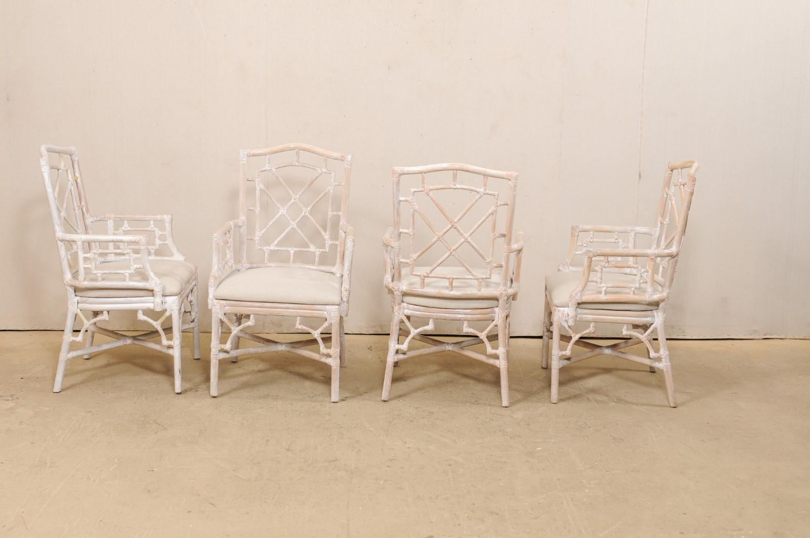 A set of four American-made faux-bamboo wooden armchairs with upholstered seats. This vintage set of Hollywood Regency inspired occasional chairs have wood frames, which have been carved to mimic the design of bamboo. The faux bamboo is crossed