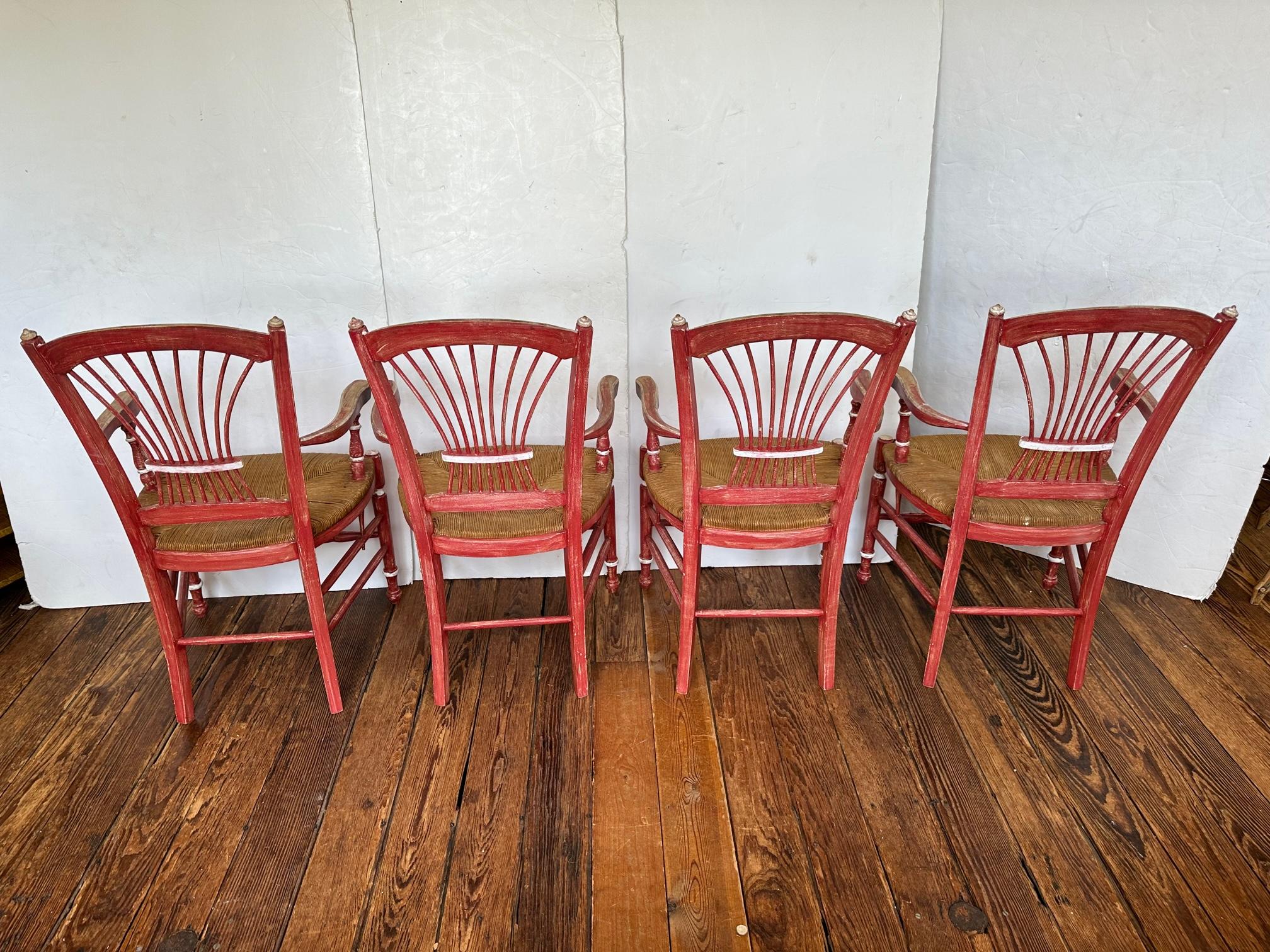 Set of 4 French Country dining chairs, all of them arm chairs, having wonderful spindle wheat sheaf style backs and natural rush seats.  They are painted a red rasberry with an antiqued finish and silver detailing.