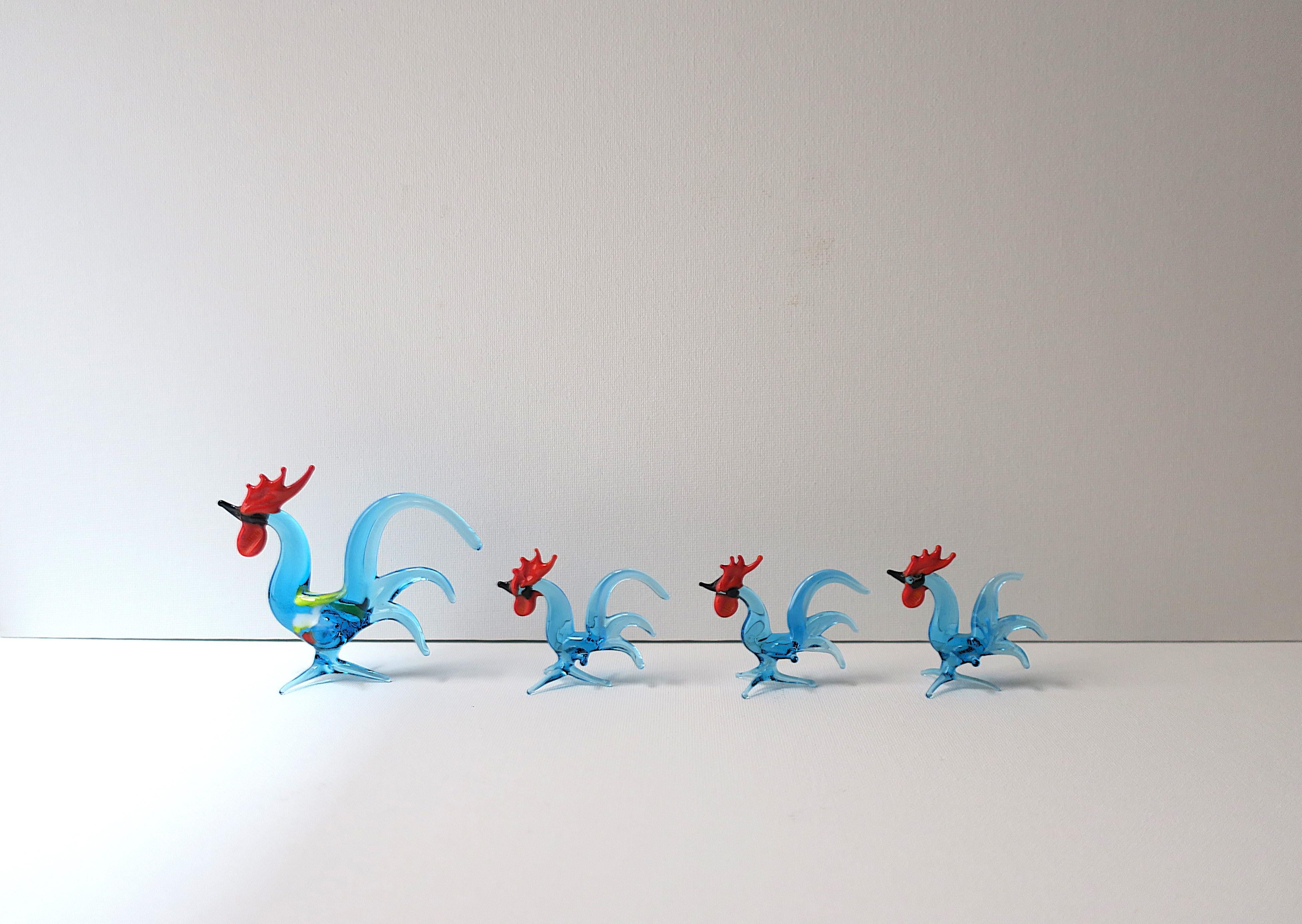 Magnifique ensemble de 4 sculptures de famille de coqs en verre d'art fait à la main, vers les années 1970. Quatre (4) coqs en set, verre soufflé, fait à la main. Les couleurs du verre d'art comprennent le bleu, le noir, le rouge et une touche de