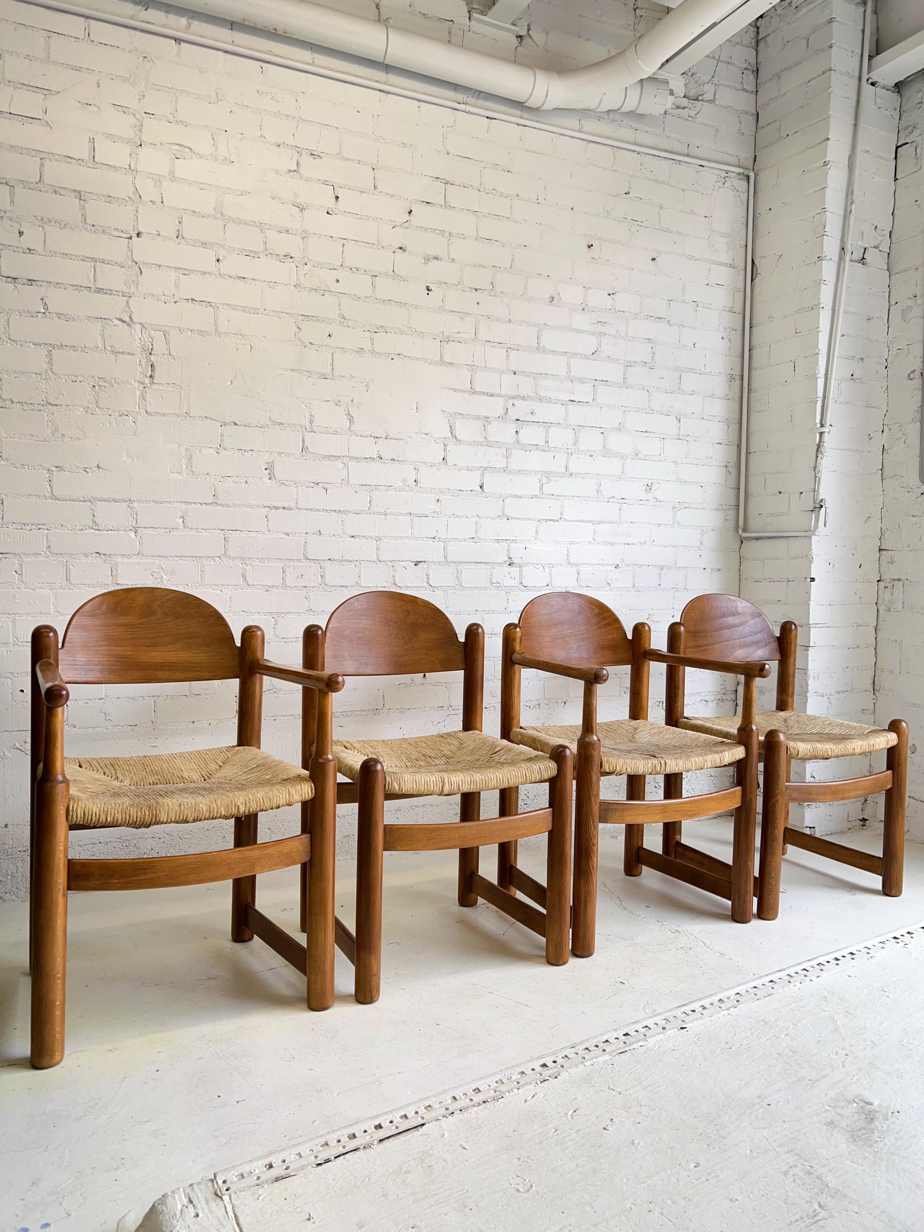 A set of 4 Hank Lowenstein’s “Padova” dining chairs in cherry wood with rush seats. Two chairs have armrests, two do not. Beautiful rounded edges, warm tones, and strong grain presence. Rush seats have some staining but are structurally sound. Made