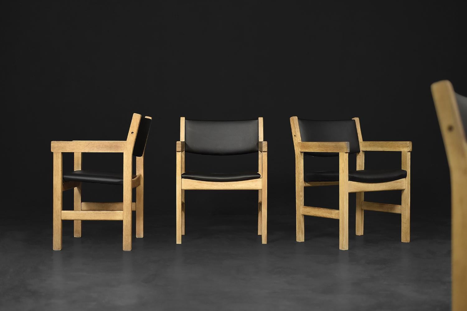 This set of four chairs was designed by Hans J. Wegner for the Danish manufacturer Getama Gedsted during the 1960s. The raw, geometric frame of the chair is made of light oak wood. The seat and backrest are upholstered with high-quality black vinyl.