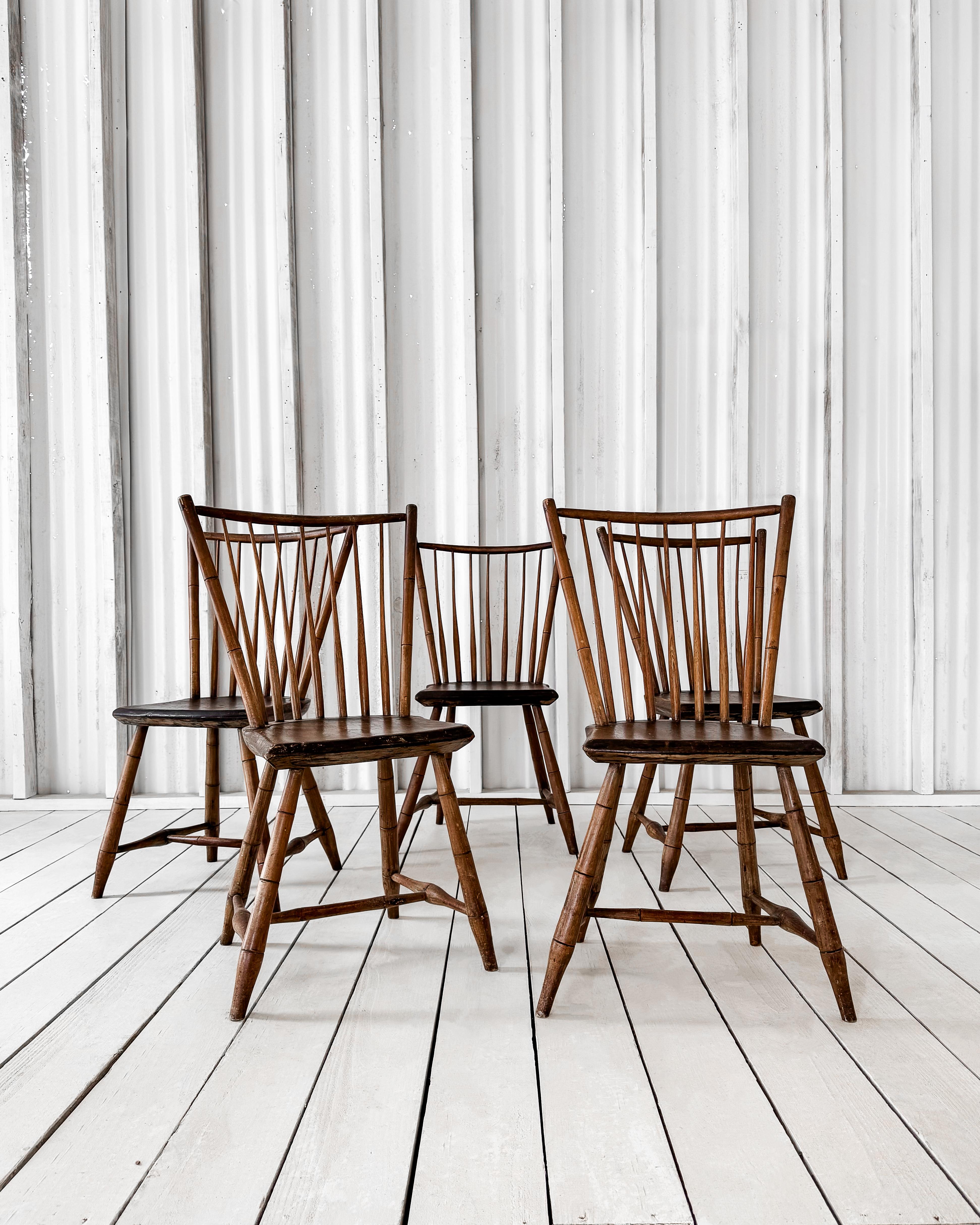A set of five 19th-century spindle-back chairs exemplifying simple yet enduring craftsmanship. Each chair features a gracefully curved top rail and slim, evenly spaced spindles that provide support and visual appeal.

The well-worn wooden seats and