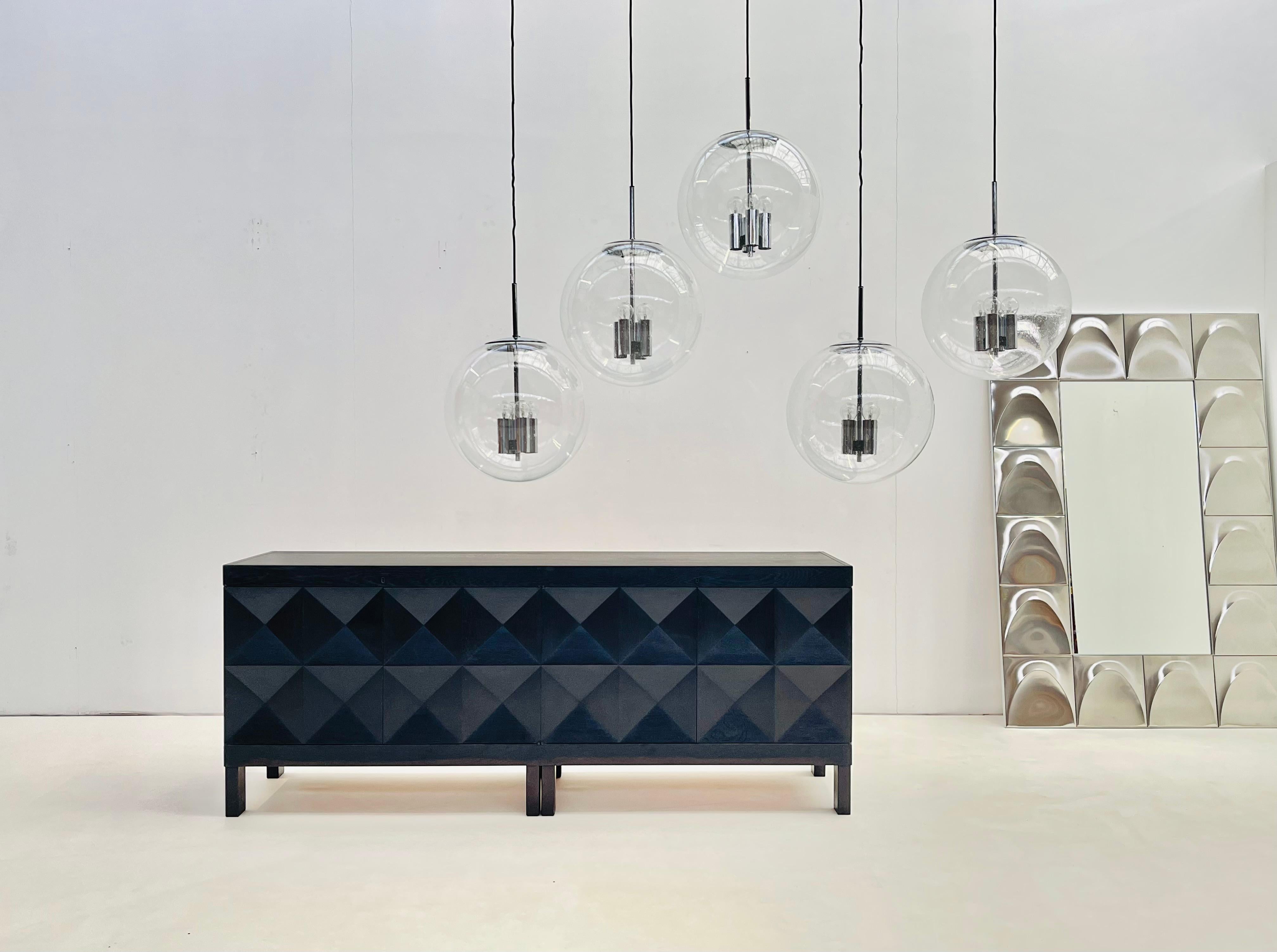 Set di 5 sfere di vetro a bolle illuminate da 4 lampadine ciascuna in eleganti prese cromate. 

Disponibile al pezzo o per il set completo. 

Questi ciondoli richiamano lo stile Art Deco in modo più moderno e brillante. Le bolle intrappolate nel