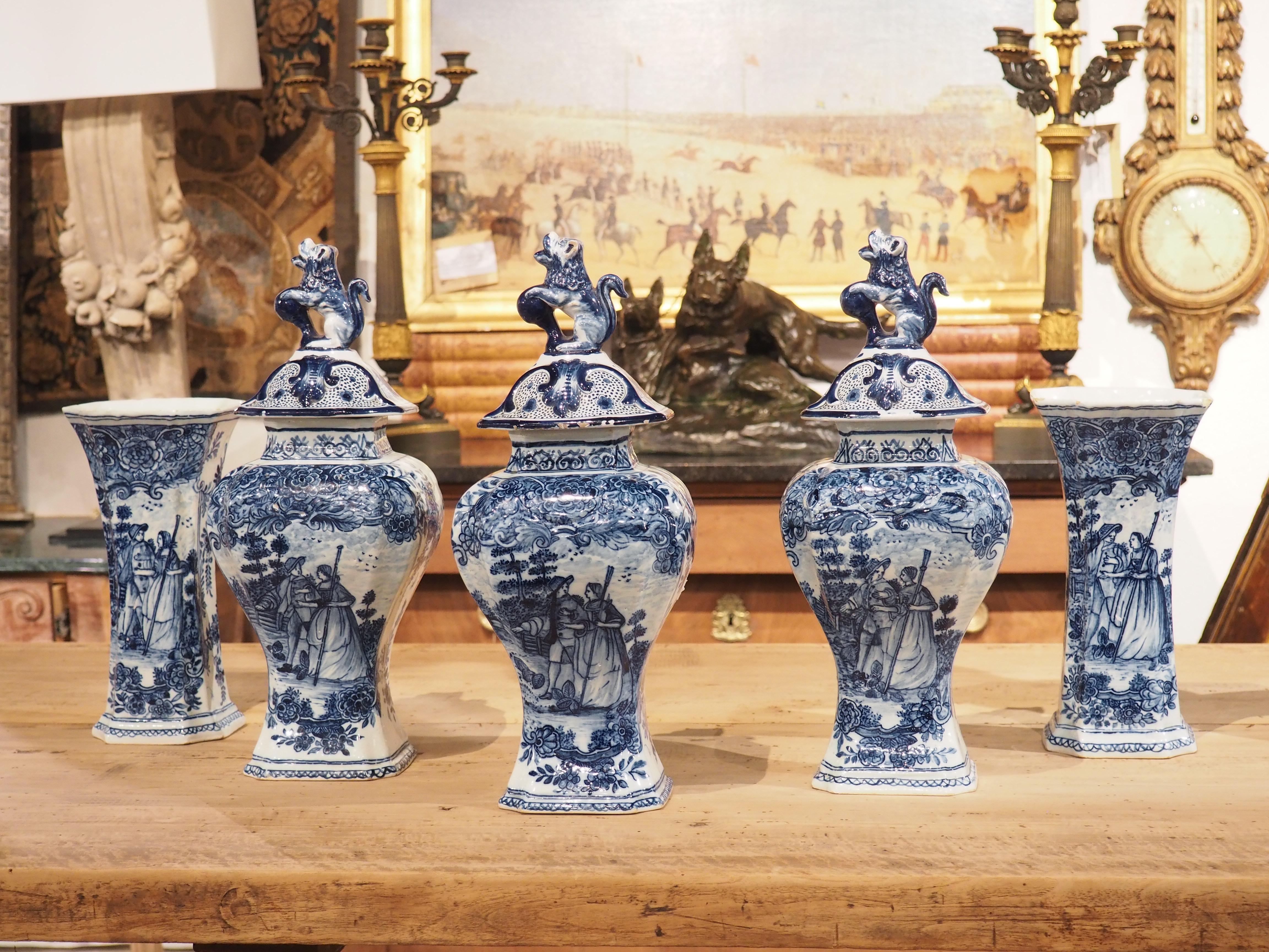 A beautiful set of five blue and white Delft vases, this faience collection was hand-painted in Holland, circa 1900. The three bulbous vases are lidded, each with a finial depicting a rampant lion with a ball in its forepaws. Beneath the lion is a