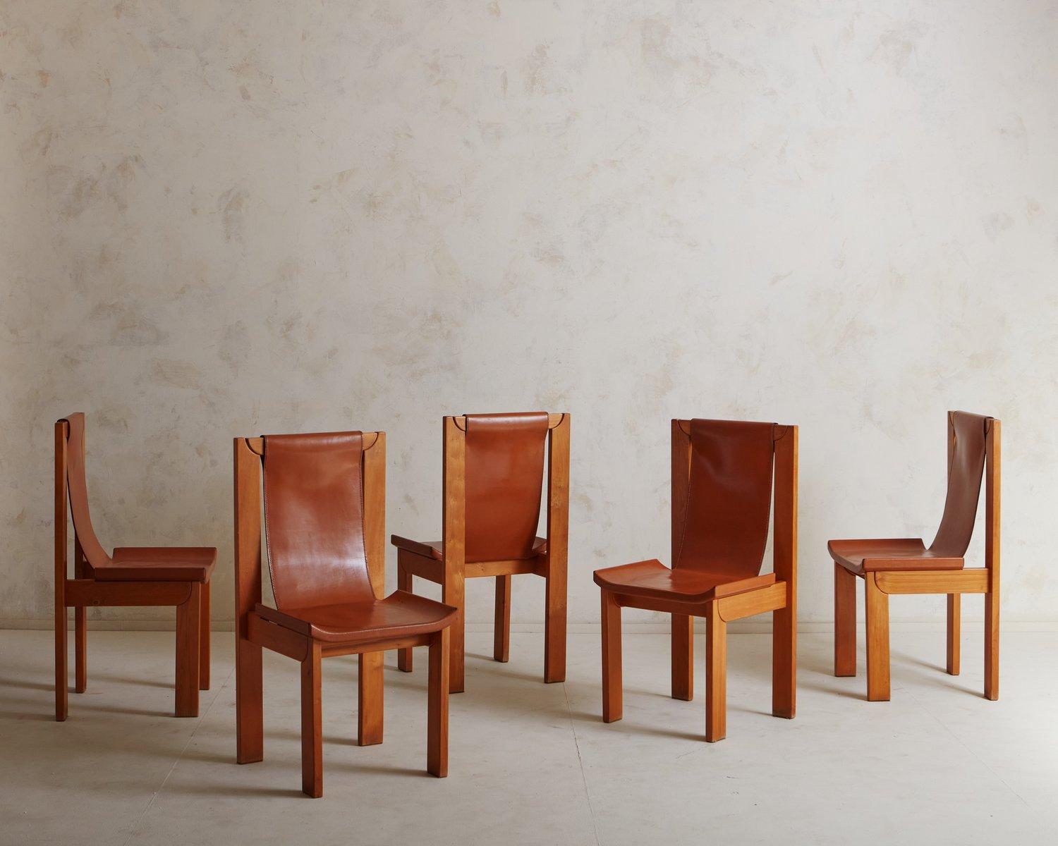 A set of 5 mid -century dining chairs with elegant elm wood frames. These chairs feature patinated cognac leather seats and sling backs with stitch detailing. The seats have subtly curved edges which sit just above the frames. We love the angular