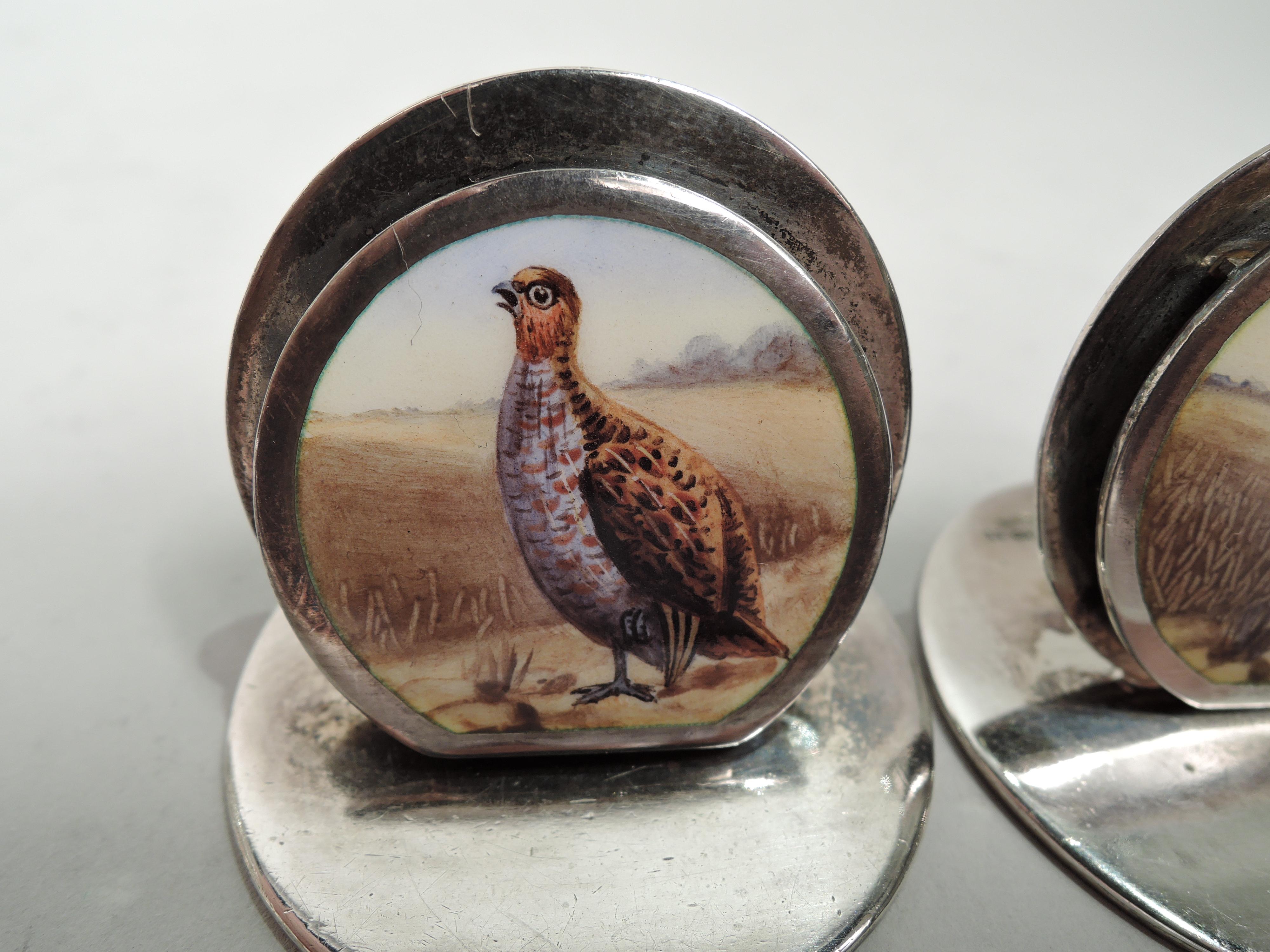 Set of 5 Edwardian sterling silver and enamel place card holders. Made by Sampson Mordan in Chester, 1904-8. Each: Two graduated discs of which the front decorated with grouse standing stiffly, alert to danger; landscape background varies. Flat