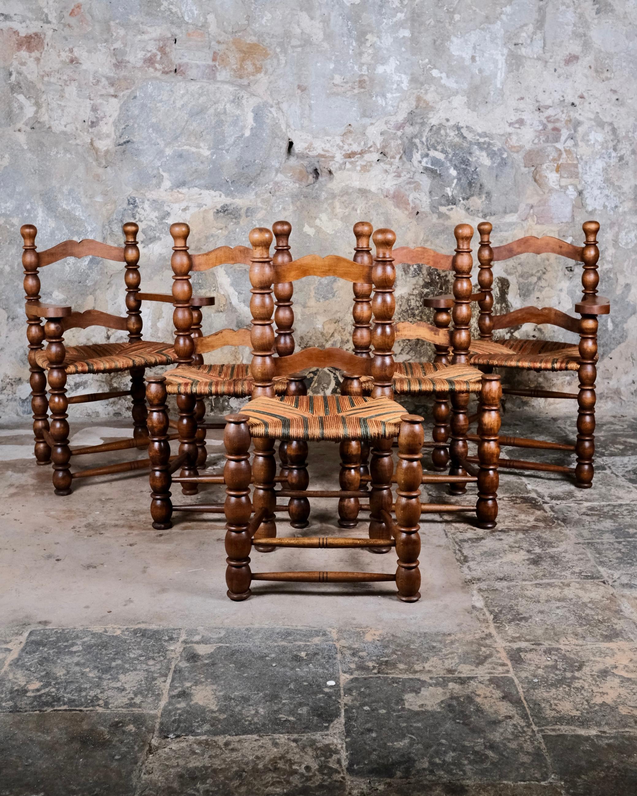 An exceptional and rare set of five French bobbin turned chairs dating from the 1940s–1950s, crafted in solid oak with vibrant multicolored straw seats. Inspired by the distinctive design language of Charles Dudouyt, these chairs are a celebration