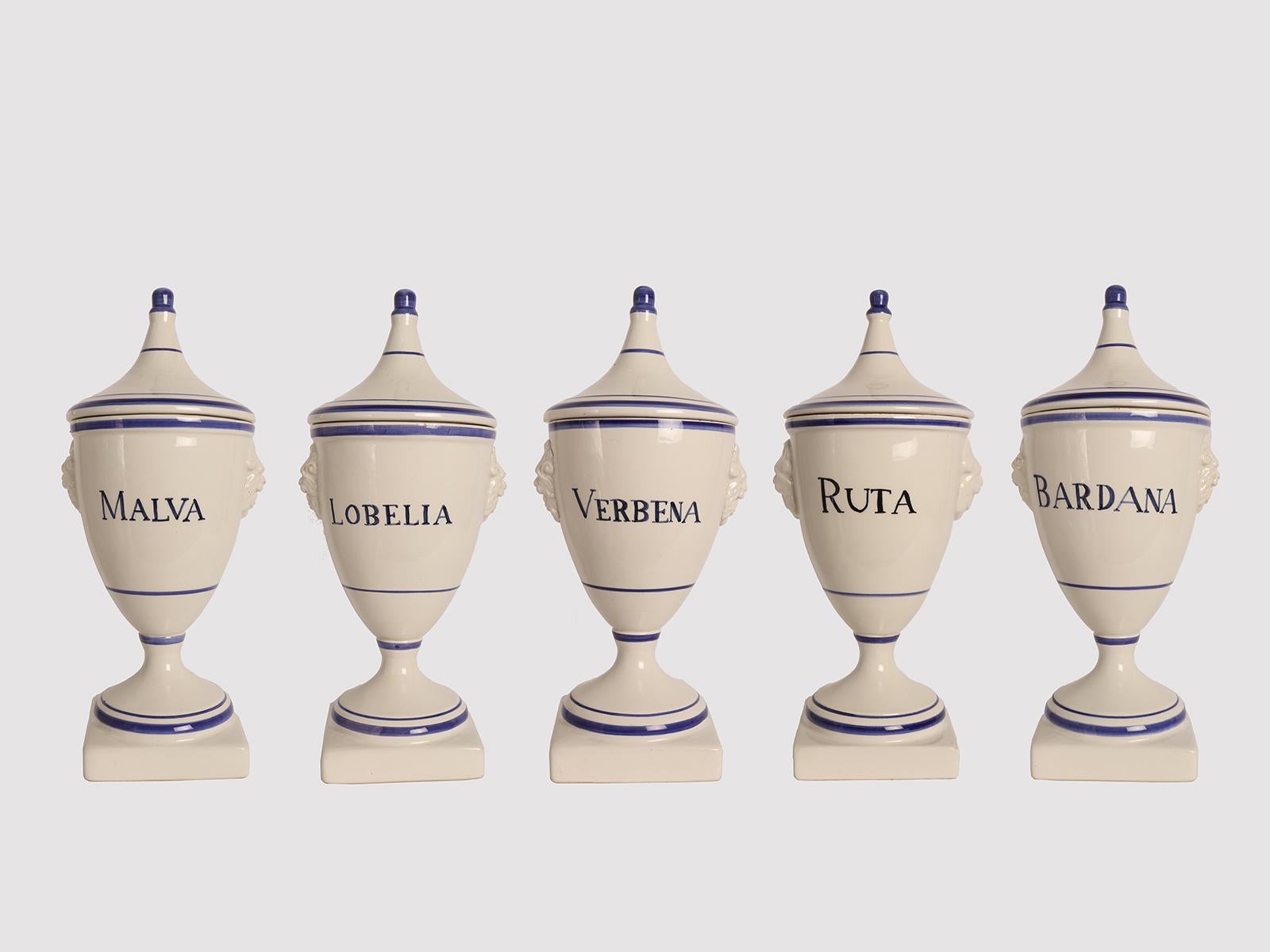 Set of five large apothecary-herbalist jars in white ceramic with cobalt blue decorations, to contain Mallow, Lobelia, Vervain, Rue, Burdock of neoclassical taste. The handle of the lid is in the shape of a stylized acorn, on the sides of the vase