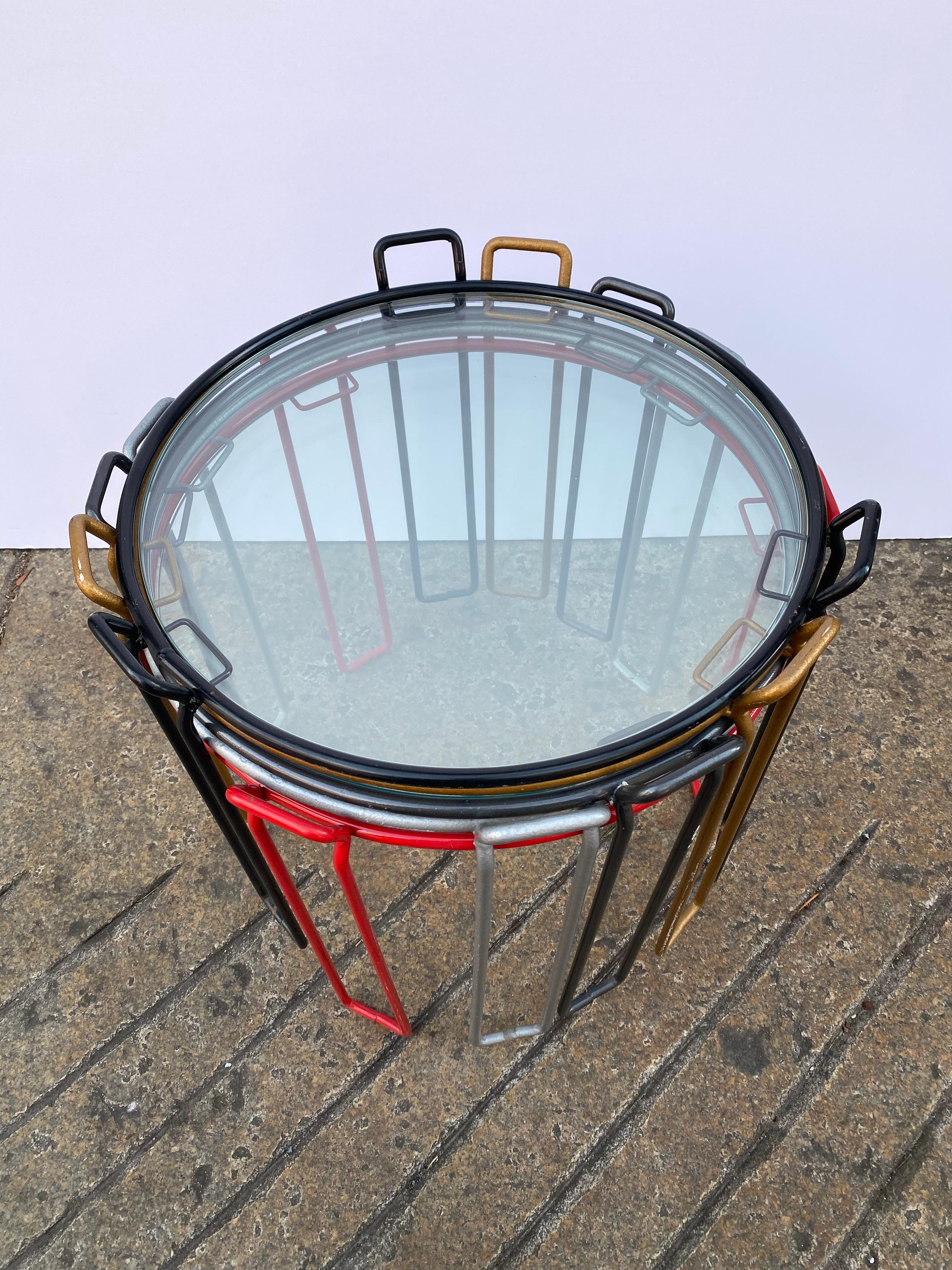 Versatile set of 5 stacking iron and glass tables. Iron frames are painted colors: 2 black, 1 red, 1 copper, & 1 grey.