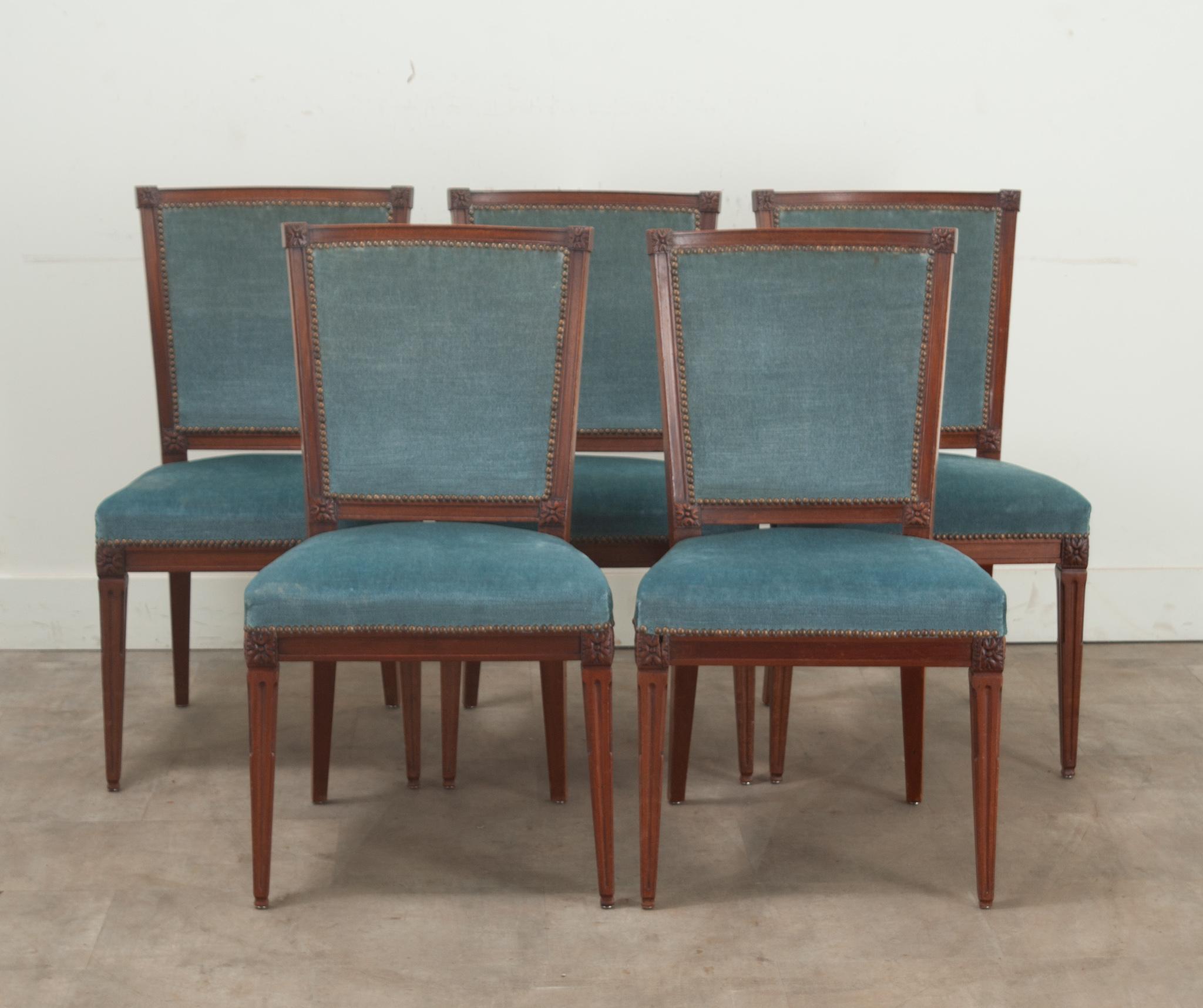 A classically designed set of Louis XVI style dining chairs from France. The oak frames feature rosette carvings on the back and seat corners and brass nailheads keep the gently used blue mohair fabric upholstery in place. The comfortable chairs are