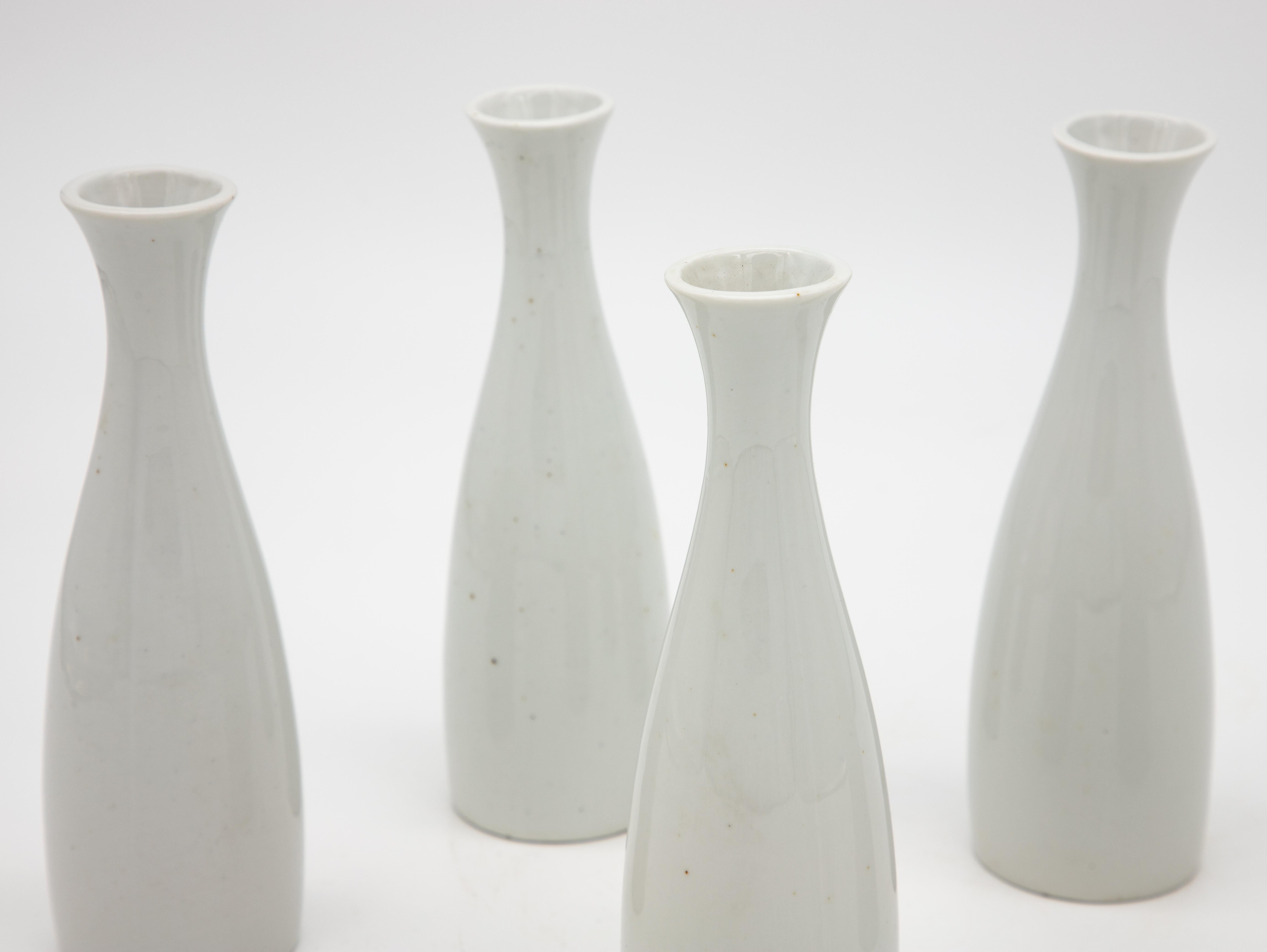 A set of five white ceramic bud vases. Green maker's mark on the bottom reads 