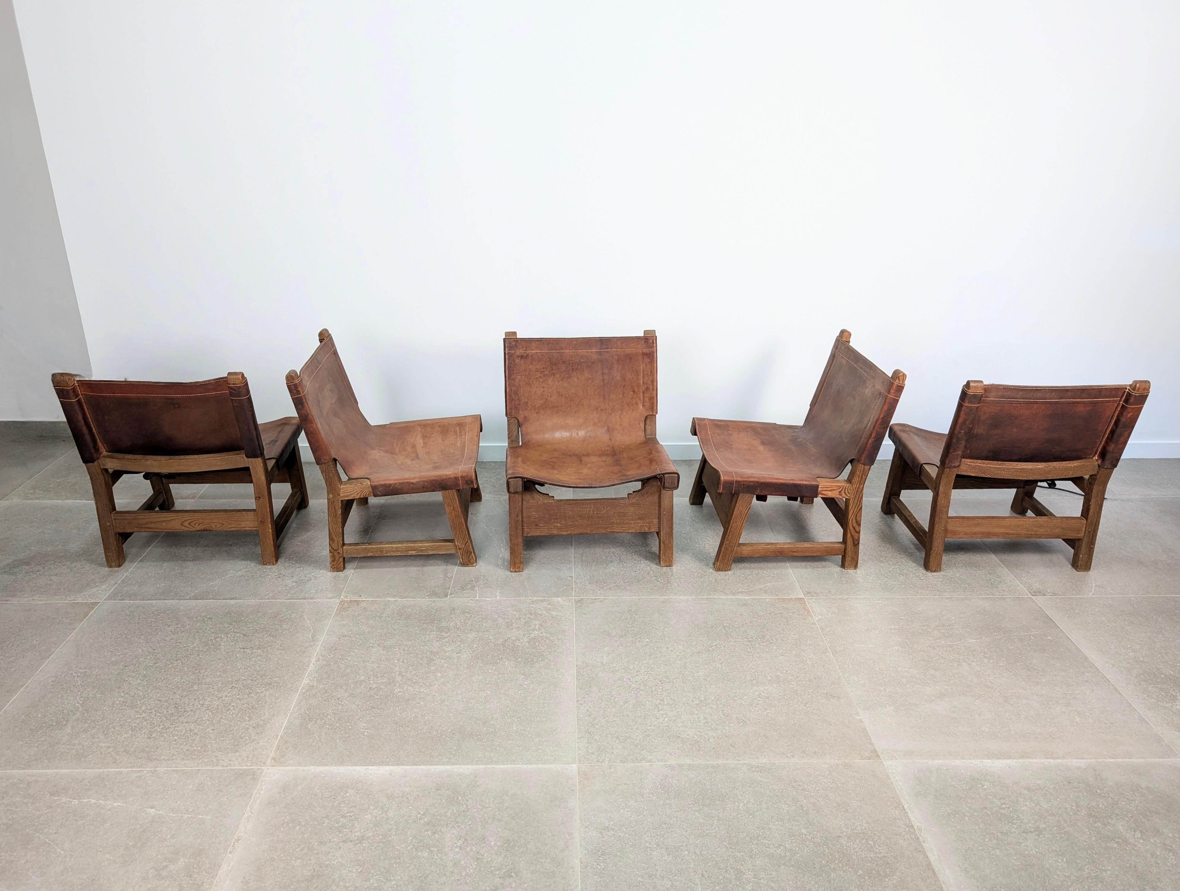 Exceptional set of five Spanish chairs from the 1960s, crafted in solid oak with original thick saddle leather seats and backs. Their bold and architectural structure, with square lines and exposed tenon joints, reflects the artisanal mastery of