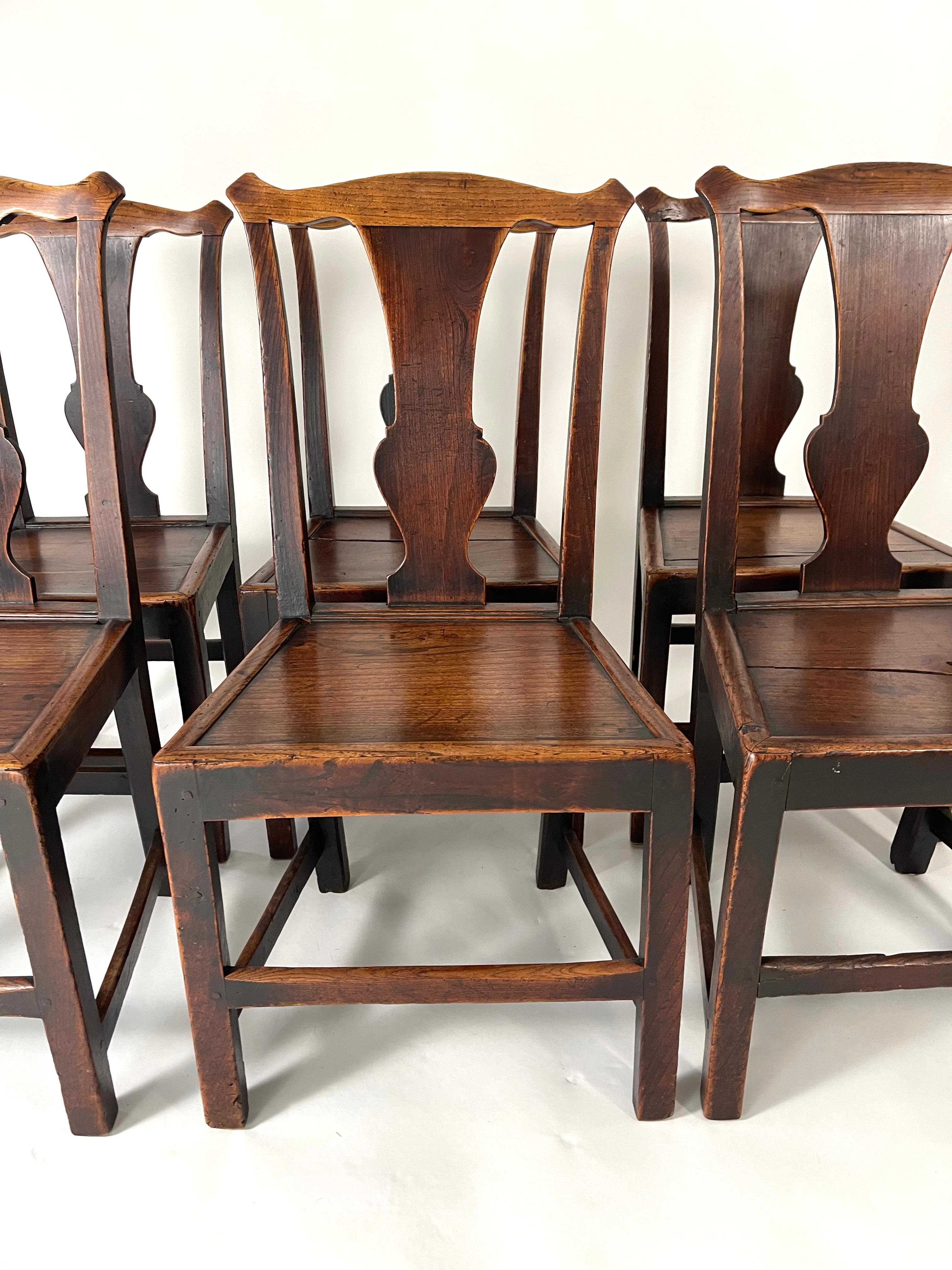 A set of six 18th century Chippendale English Provincial dining chairs in elm and oak. Bold, simplified form with wonderful patina and character, the shaped crest rail above vasiform back splats and solid plank seats supported by square section legs