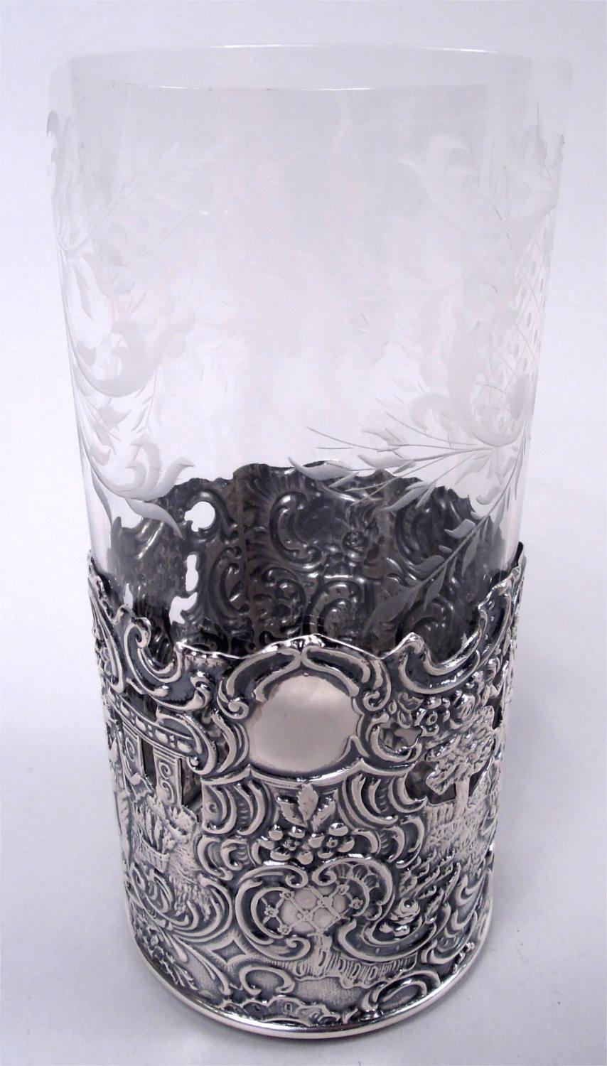 Set of 6 Hanau-style sterling silver highball holders, ca 1910. Each: Cylindrical with open bottom. Dense repousse scrolls, flowers, and colonnades populated with pipers and strummers and a lone lady importuned by a cherub. An American adaption of