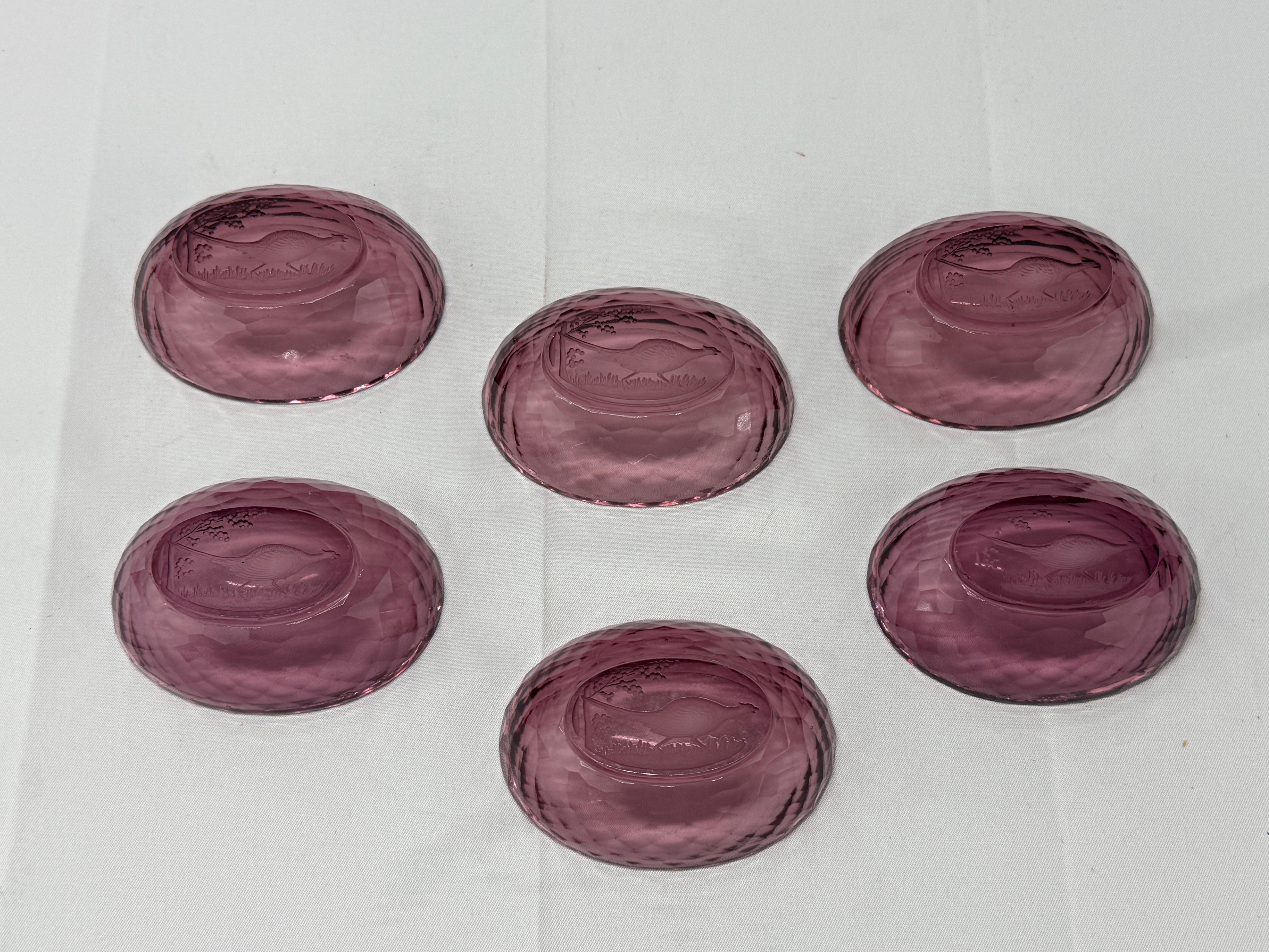A set of six exquisite amethyst glass open salt cellars, each featuring finely detailed intaglio-cut pheasant motifs. The deep, rich hue of the amethyst glass is beautifully enhanced by the intricate craftsmanship, showcasing a delicate interplay of