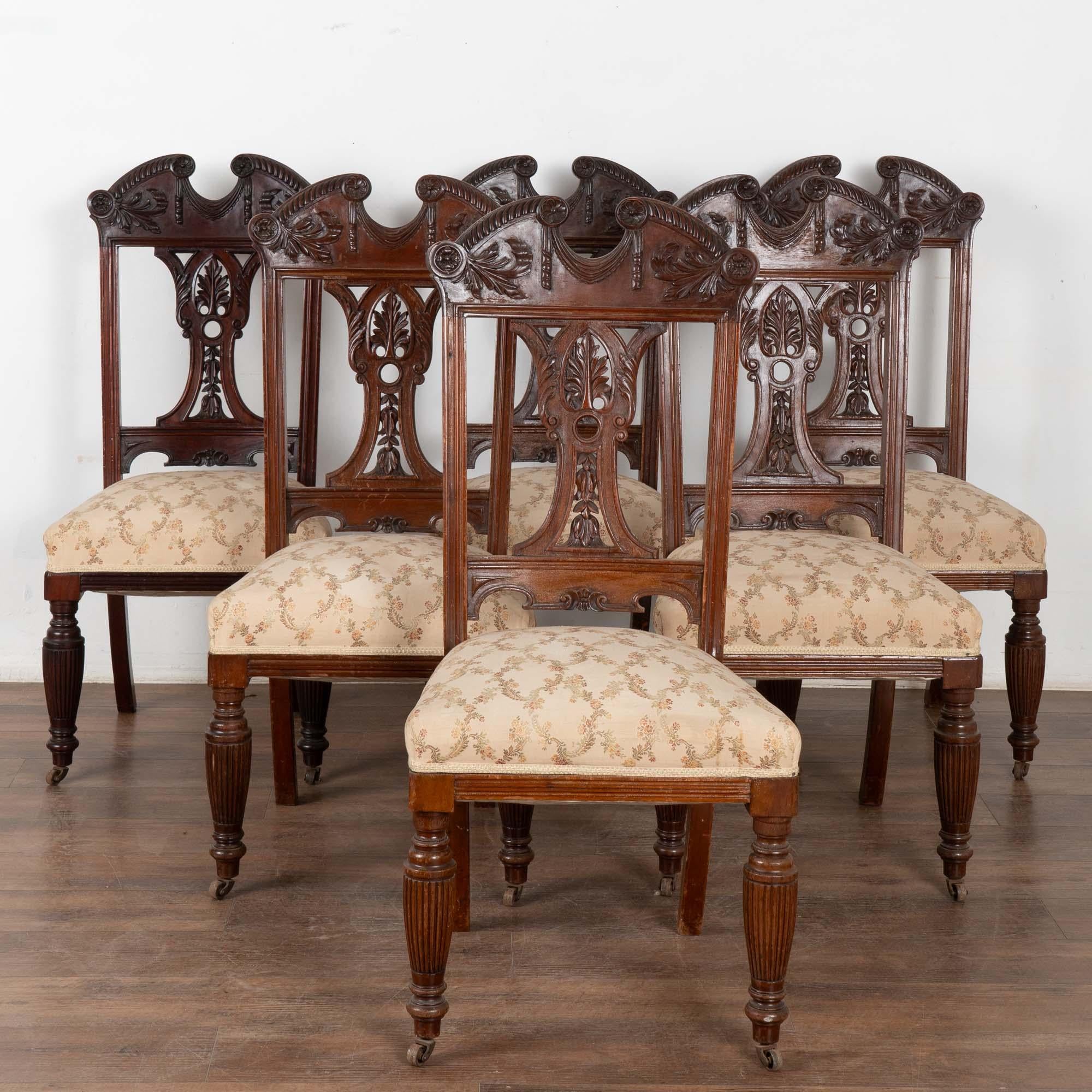 This set of 6 antique English dining chairs are made from mahogany and come with upholstered seats. The choice of wood, expensive for the period, and the carved back rail, splat and turned legs make this set rather unique. The cast iron casters are