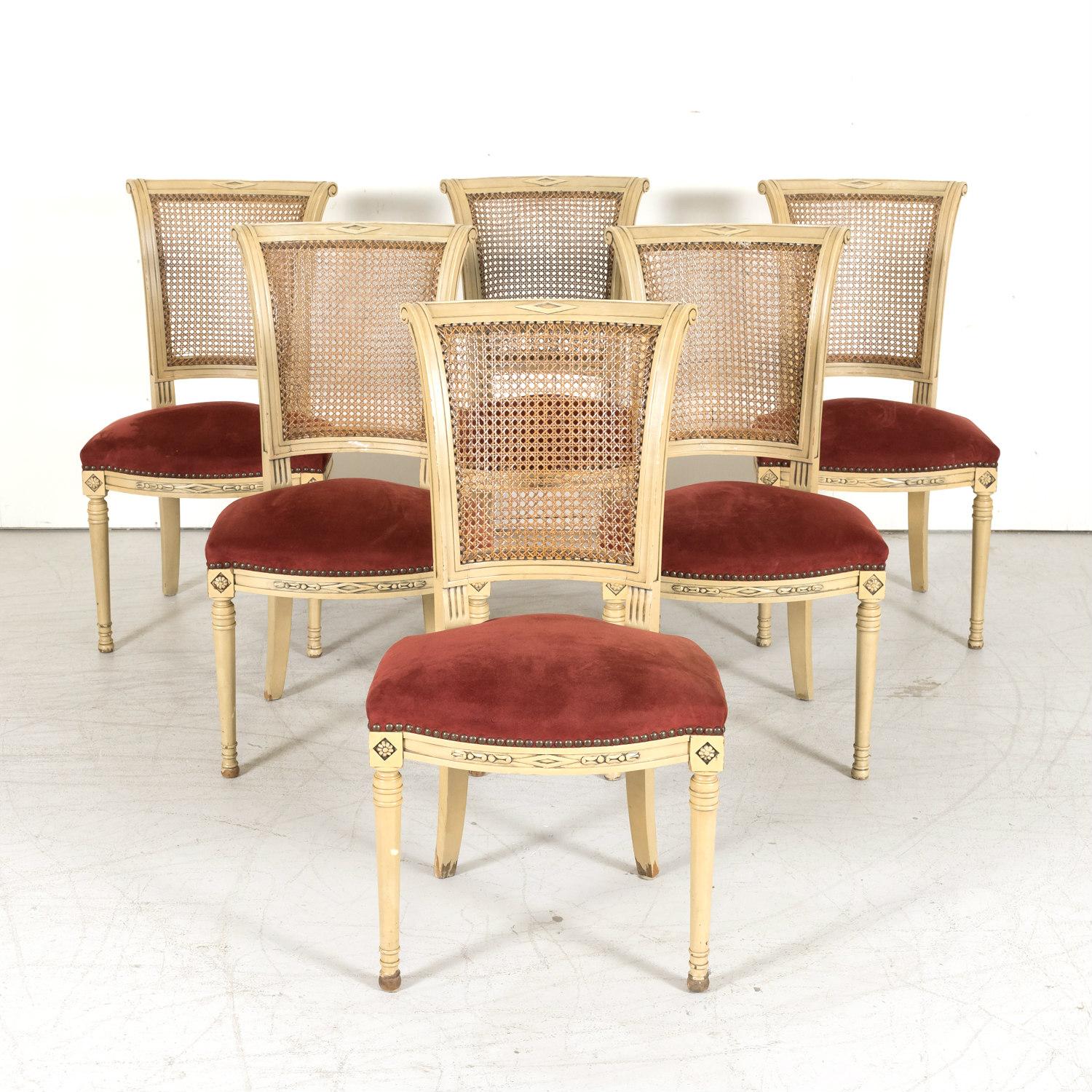 A handsome set of 6 early 20th century French Directoire style painted dining side chairs, circa 1920s, having hand caned backs, upholstered seats with nailhead trim, and typical neoclassical carvings. Featuring overscrolled square tapering backs