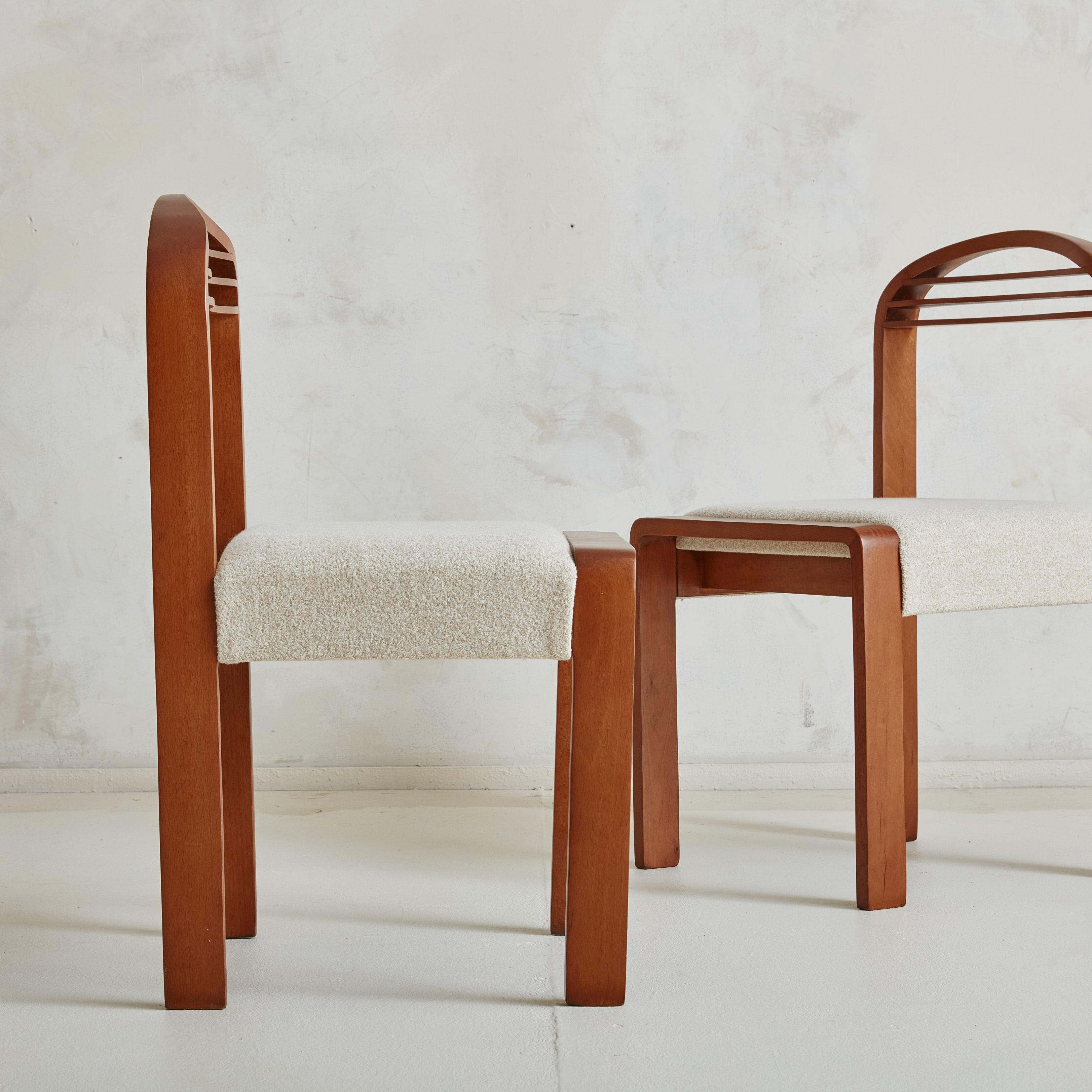A set of 6 1980s Italian dining chairs featuring bentwood frames in a rich, cherry hue with dramatically arched seat backs, horizontal line details, and rectangular block legs. The stained wood frames contrast beautifully to the cream upholstered