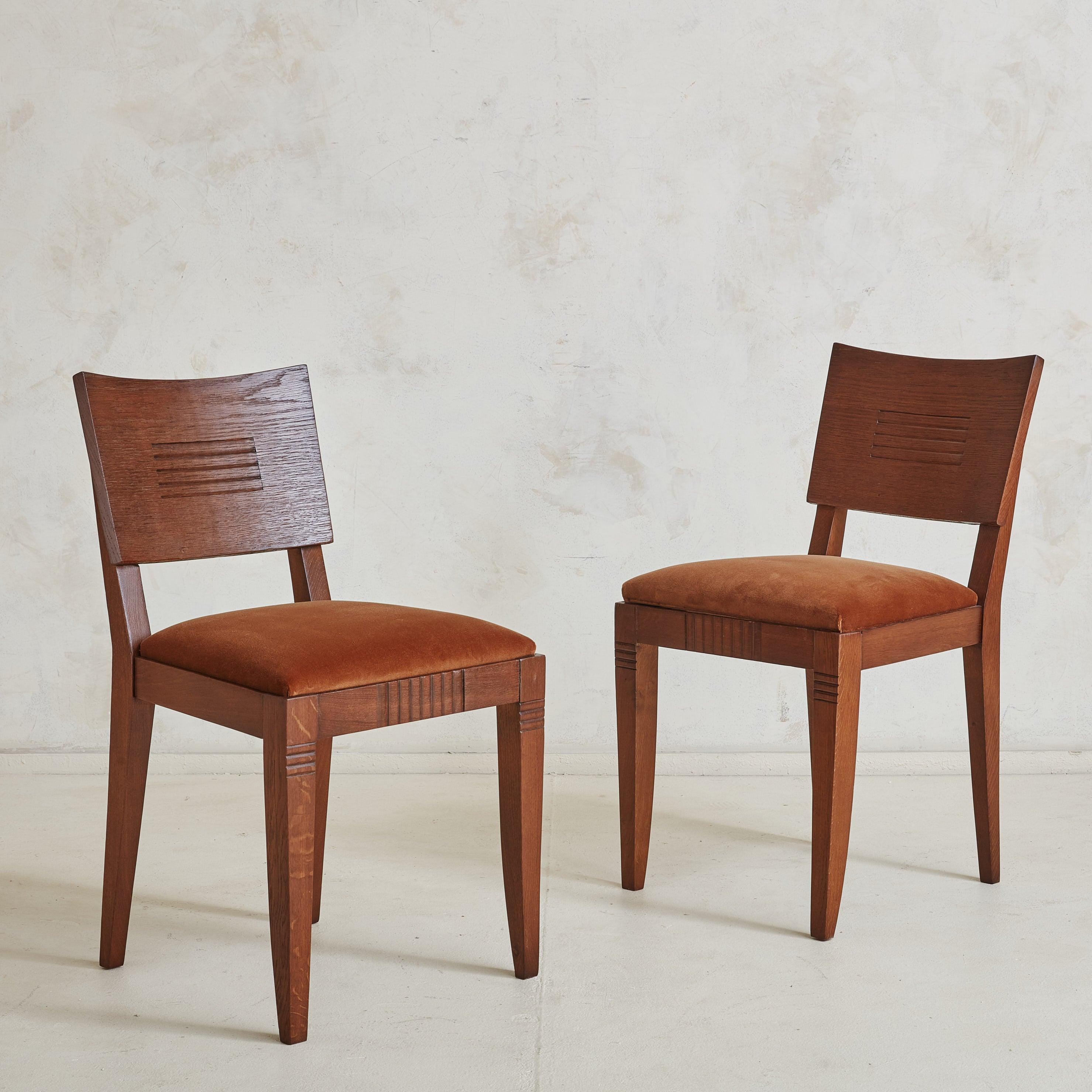 A set of 6 Art Deco dining chairs in the style of the Early 20th Century French designer, Charles Dudouyt. The beautifully grained oak frames feature elegant saber legs and curved backrests with hand carved geometric details. These chairs have been