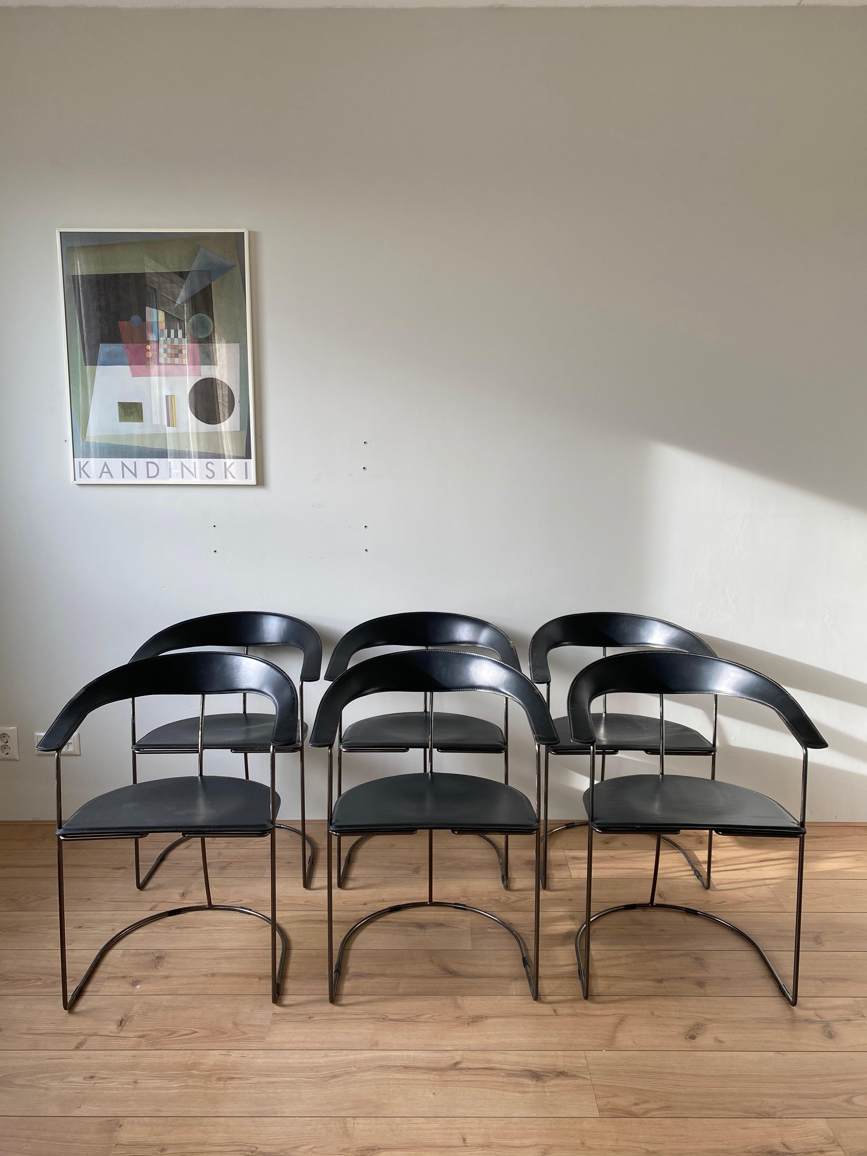 The chairs feature a gun metal finished base with thick black leather upholstery. These Postmodern and Minimalist pieces, remain in sturdy condition with some overall wear (see: images). Imprinted by the manufacturer.