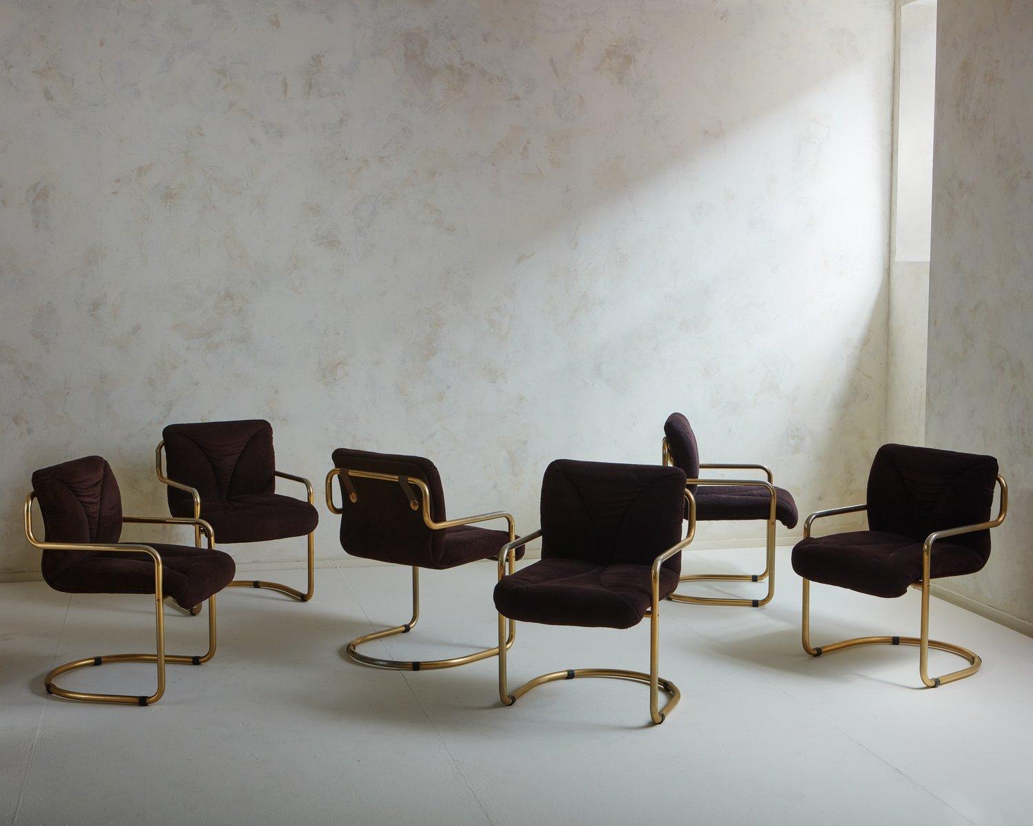 A set of 6 French mid-century dining chairs with tubular brass cantilever frames. These chairs retain their original brown upholstery with channeled detailing. The seat backs connect to the brass frames with handsome brown leather straps and