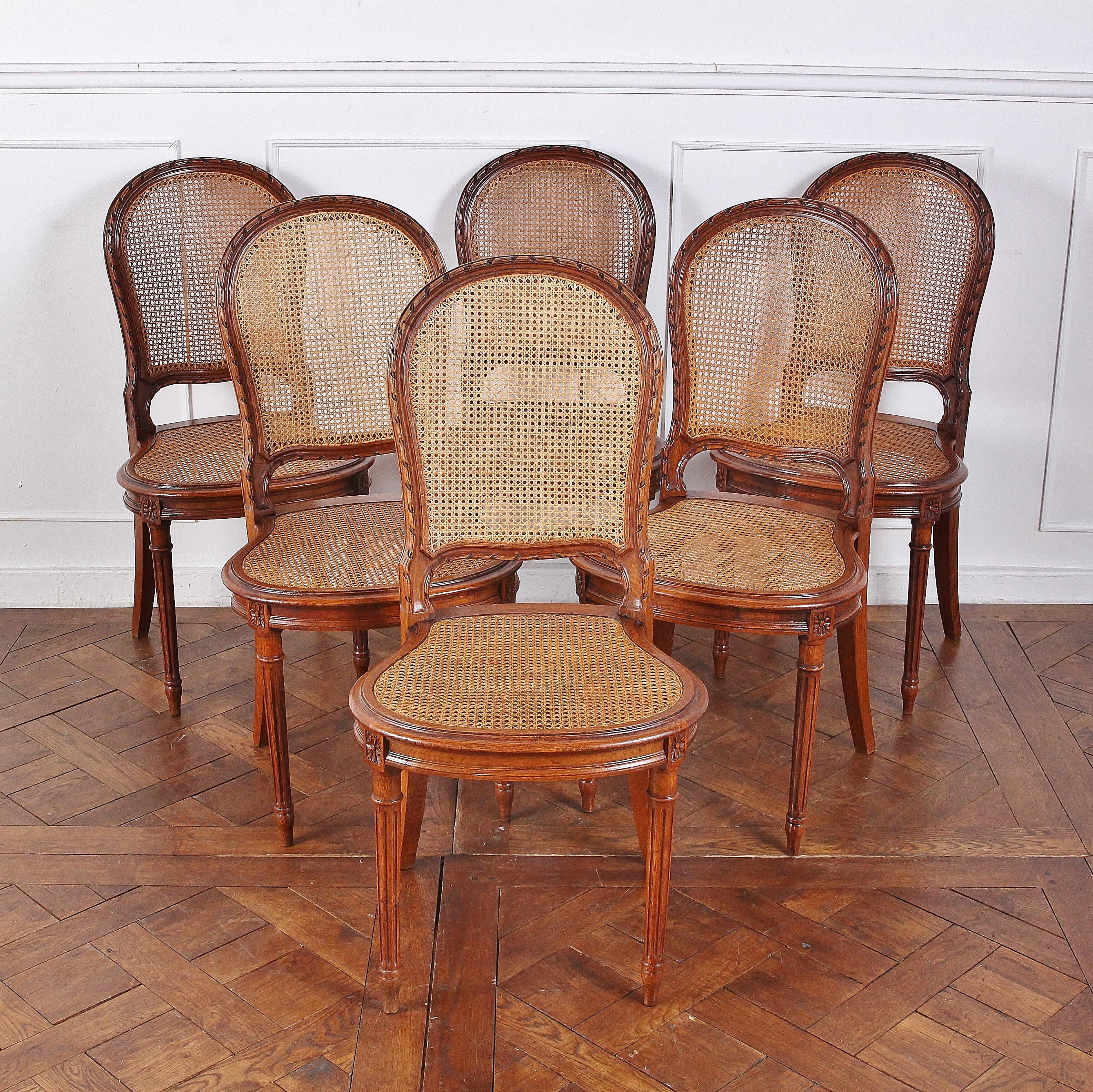 A set of six, late 19th century, Louis XVI-style chairs with cane seats and backs. The curved backs are particularly well-carved, with a fine ribbon motif along their edges; the seats are similarly rounded and raised on elegant turned and fluted