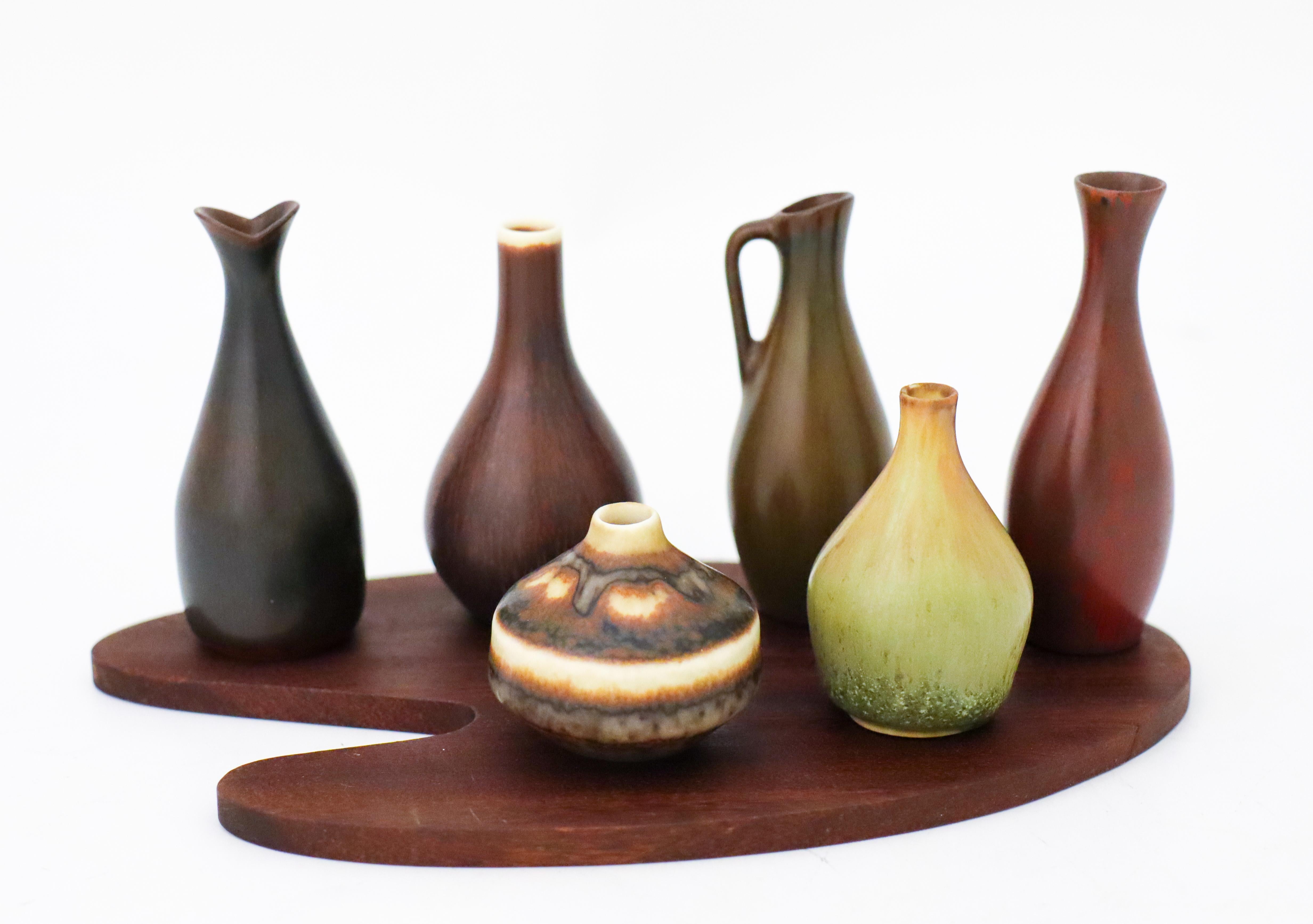 A set of 6 miniature vases on a wooden base designed by Carl-Harry Stålhane and one by Gunnar Nylund at Rörstrand, They are between 4 - 7.5 cm (1.6