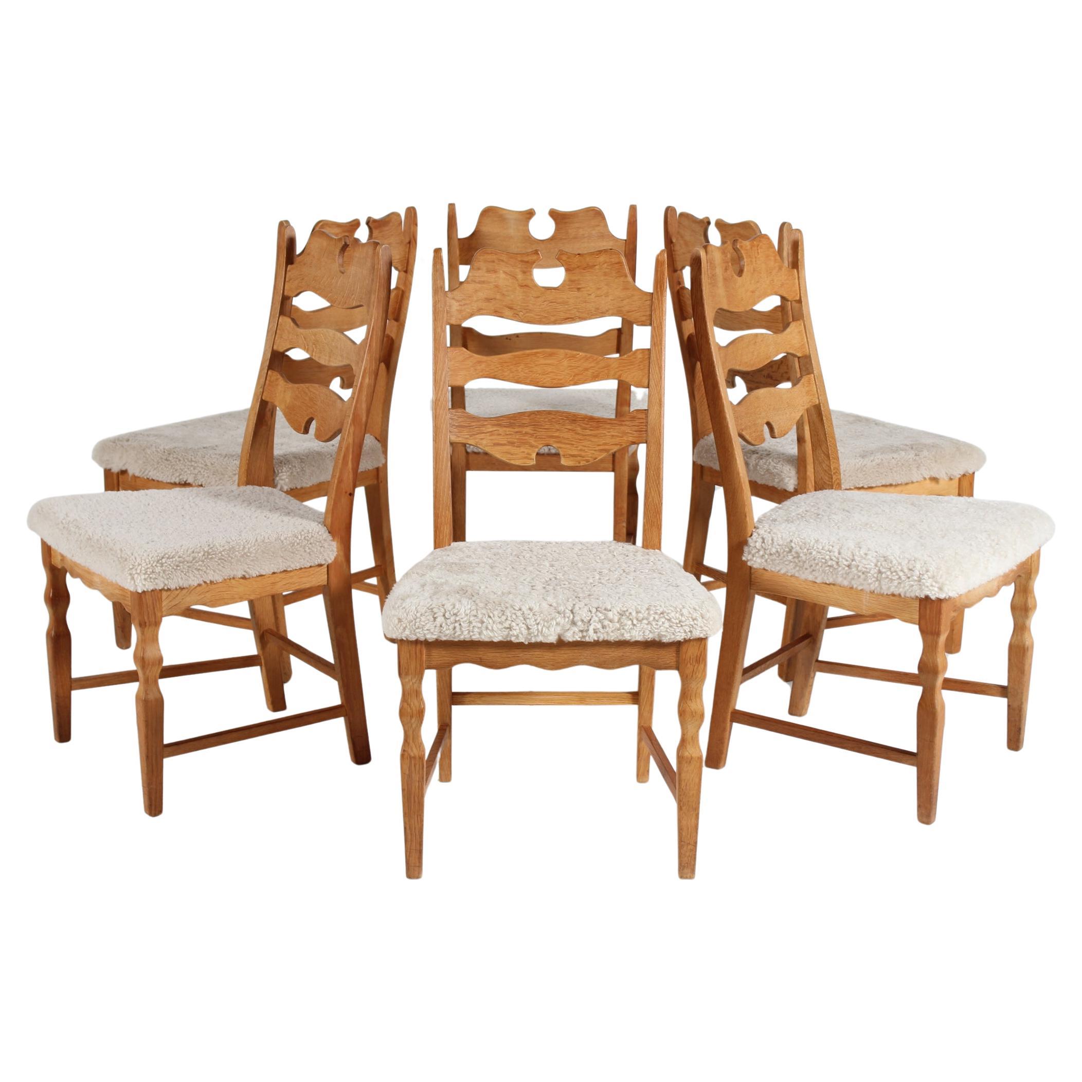 Hier ist ein Satz von 6 dänischen Vintage-Stühlen im tollen Landhausstil, entworfen von Henning Kjærnulf. 
Die Stühle sind aus massivem Eichenholz mit hoher Rückenlehne und mit neuem Schaffell gepolsterten Sitzen, auf denen man sehr bequem sitzen