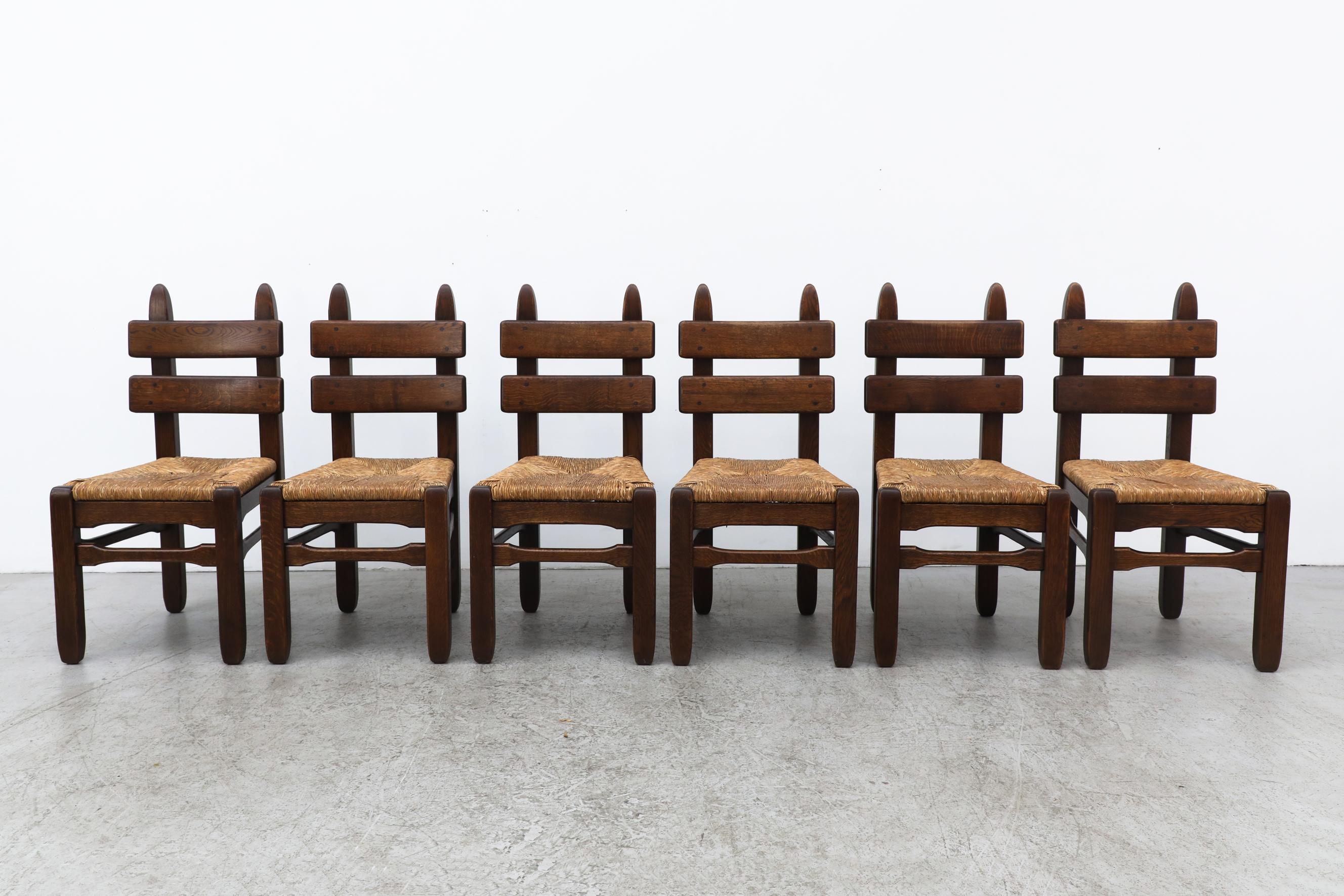 De Puydt brutalist ladder back dining chairs with rush seating. These chairs have heavy dark oak frames with woven rush seats. In original condition with a handsome patina and visible wear. There is some rush breakage on a few seats. with wear