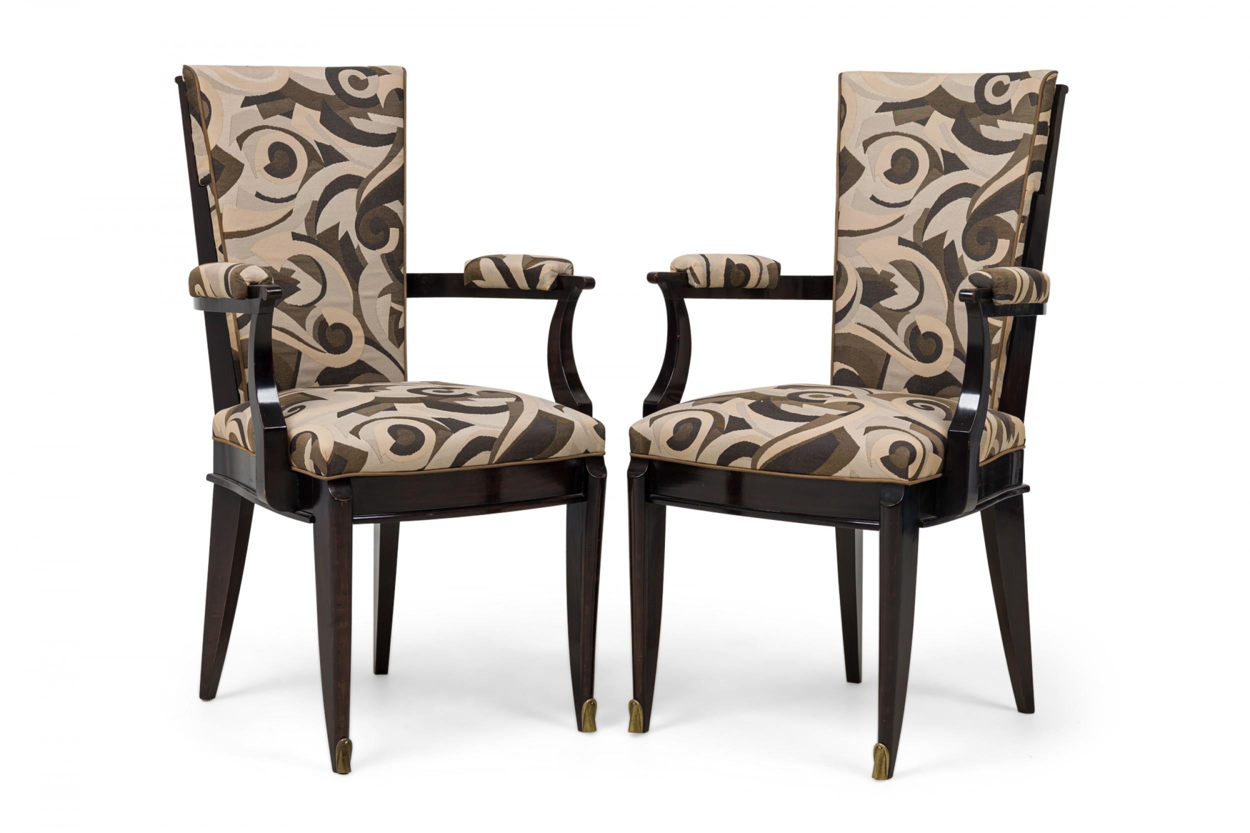 SET of 6 French Art Deco Ebony de Macassar armchairs featuring a tapered rectangular back, scroll arms with armrests, upholstered in an earth tone geometric patterned fabric with piping, molded frieze, the 2 front legs splayed with brass sabots.